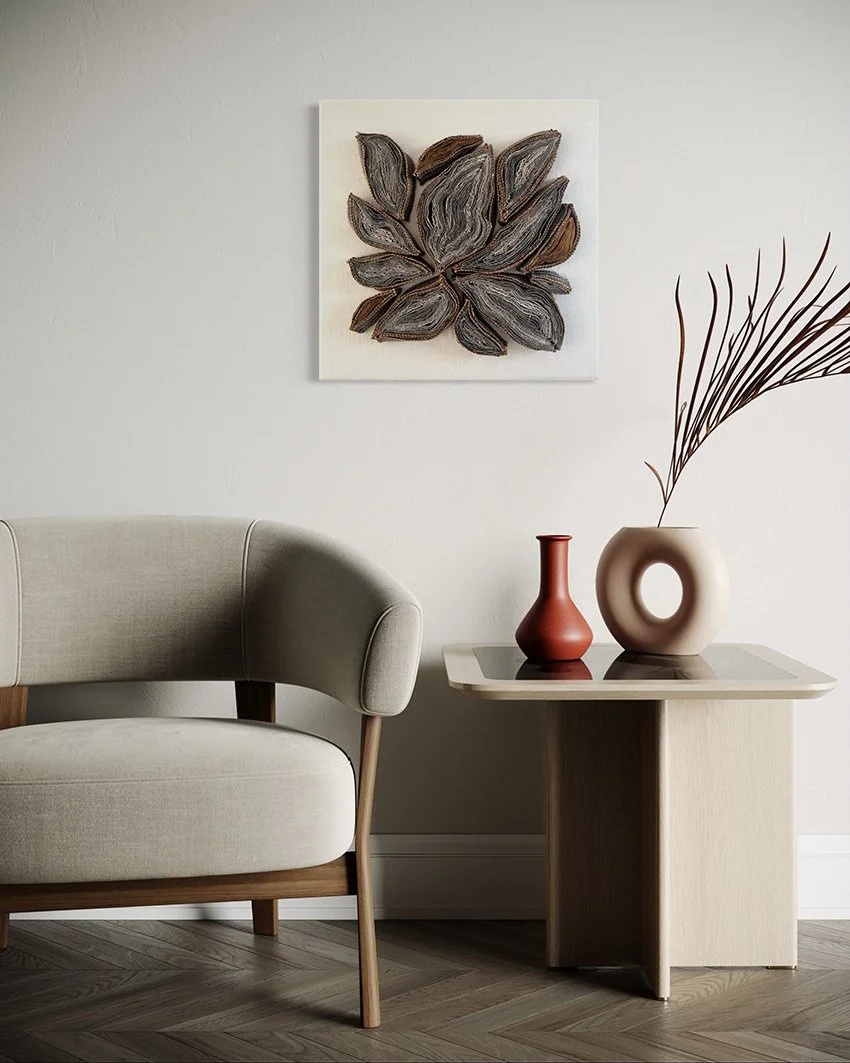 Een woonkamer met een beige bank, een houten bijzettafel met twee vazen en een gedroogde tak, en een kunstwerk met bladeren op de muur.