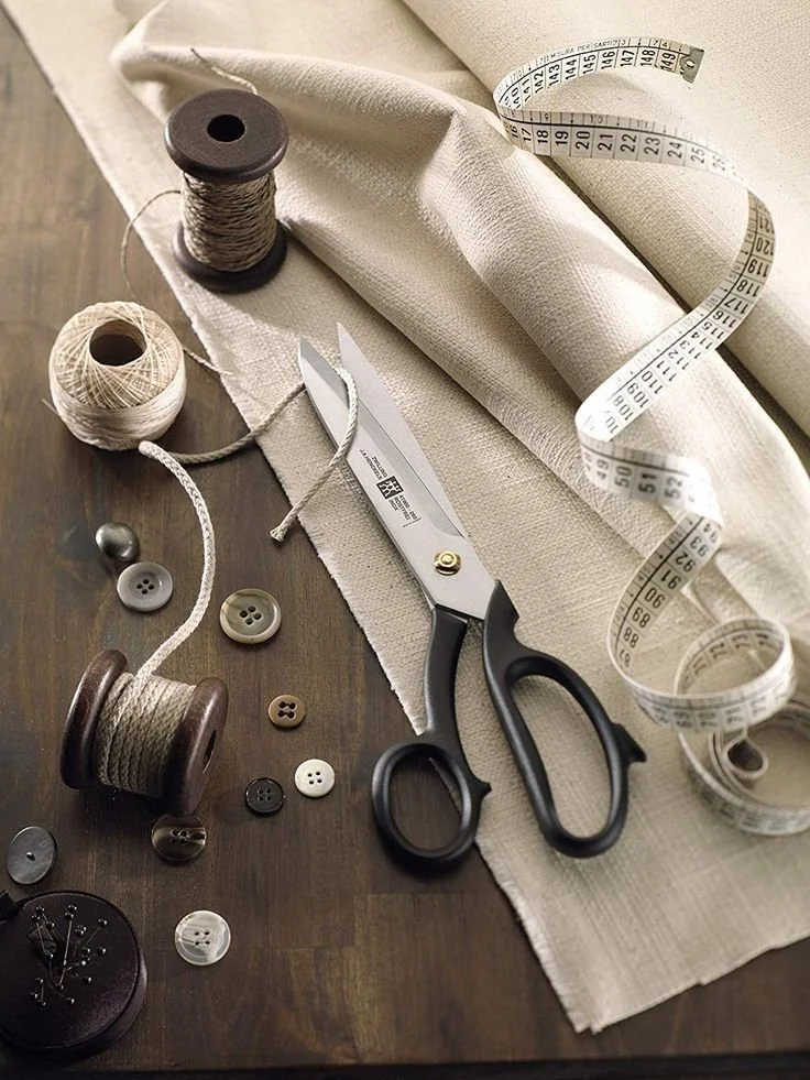 Naald en draad, schaar, knopen, meetlint, en lap stof op tafel.