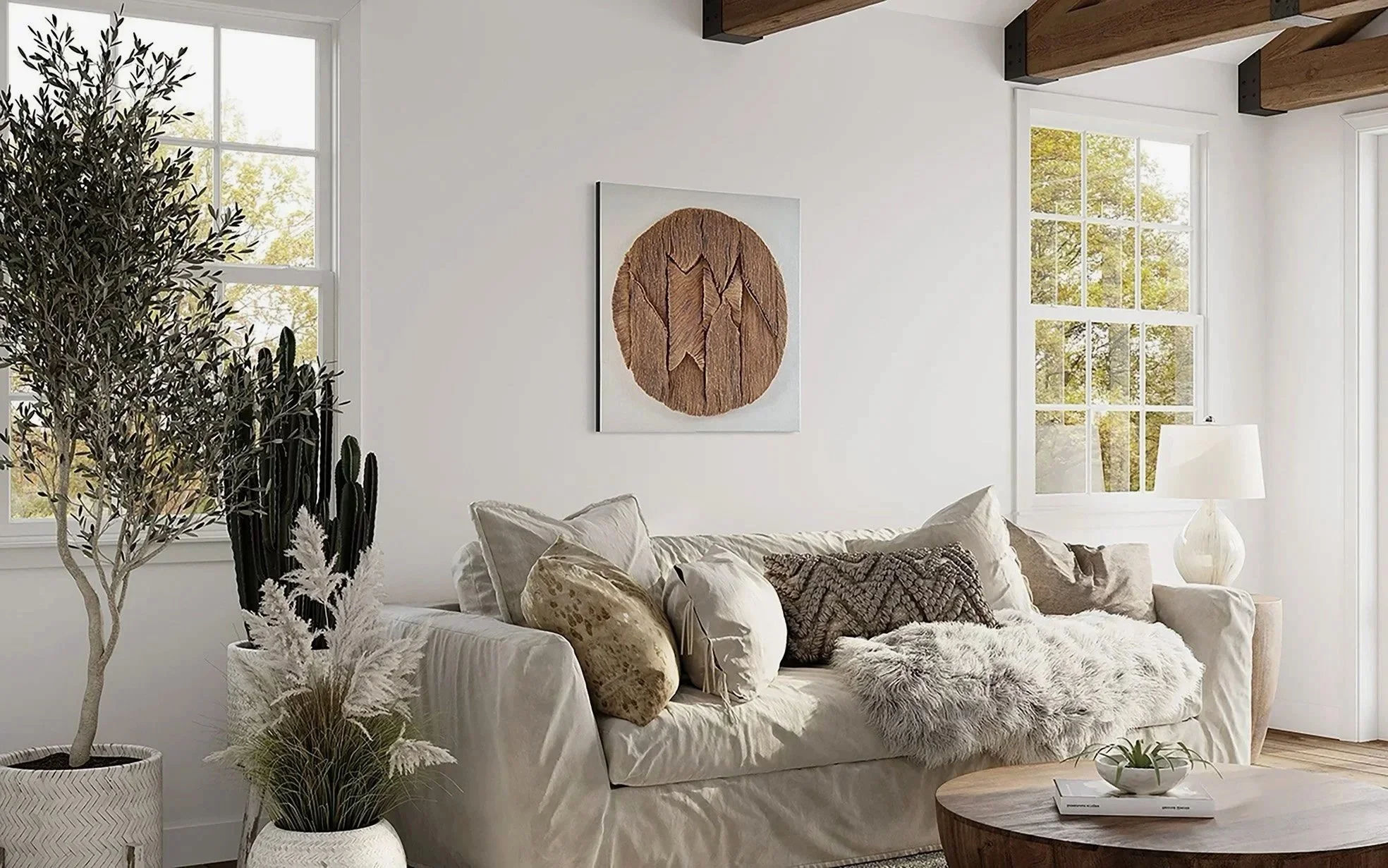 Een woonkamer met witte muren en grote ramen die natuurlijk licht binnenlaten. Een beige bank met verschillende kussens en een zachte deken, een houten salontafel met een plantenbak, een grote plant in een witte pot en een lamp met witte kap. Wanddecoratie hangt aan de muur.