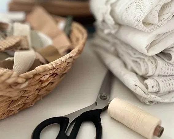 Wit gekleurde stoffen, een rol naald en draad, en een mand met stofresten op een tafel.