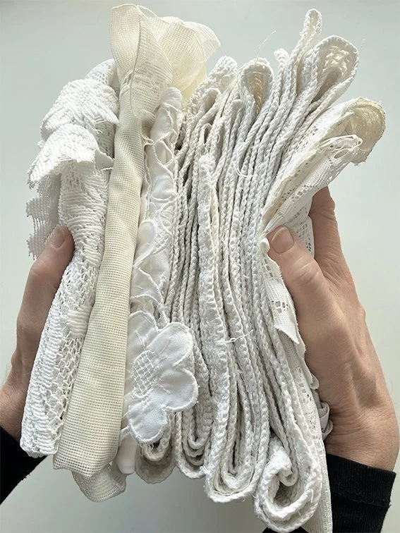 Handen die een bundel witte en crème gekleurde stoffen en naaigaren vasthouden.