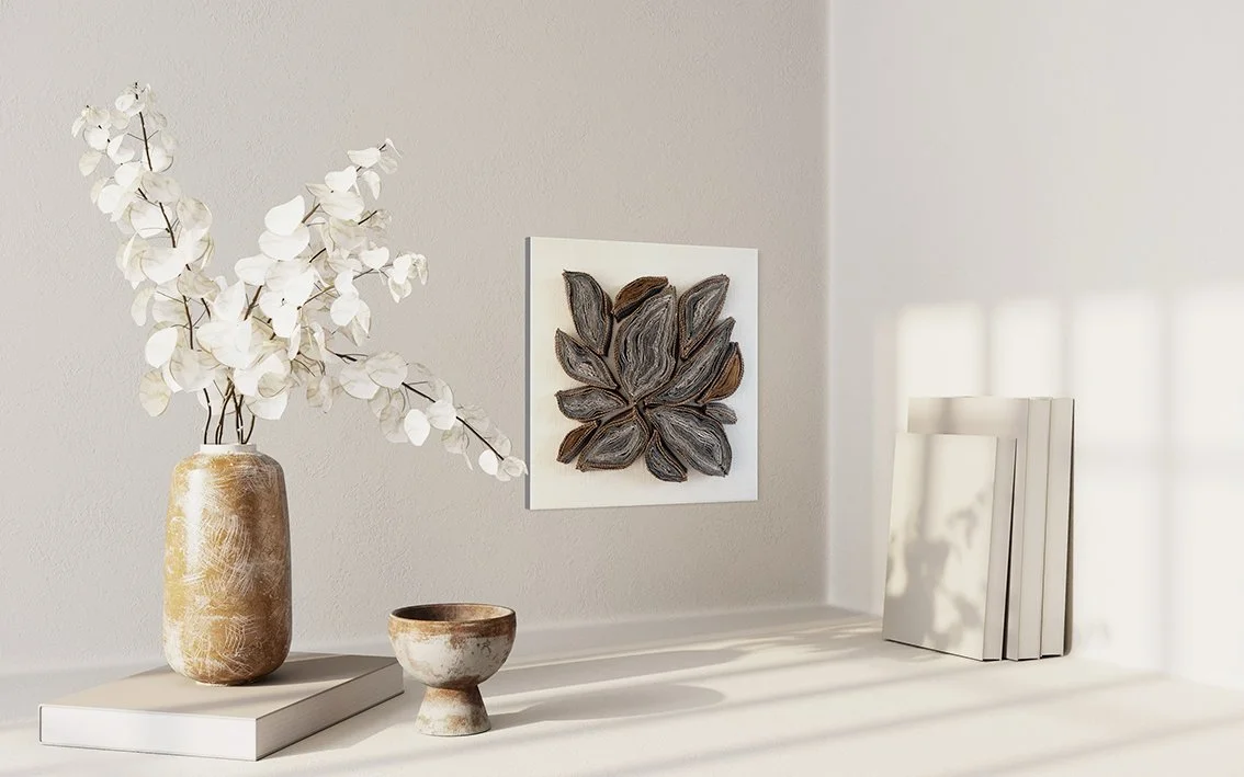 Decoratieve woonkamer met vaas met witte bladeren, keramische kom, wandkunstwerk met bloemenmotief en een stapel boeken.