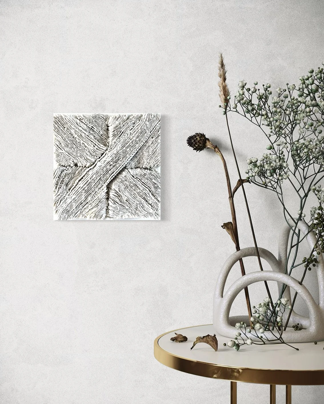 Een witte vaas met bloemen en takken staat op een ronde tafel met een gouden rand, tegenover een wit-wanden muur met een abstract kunstwerk.