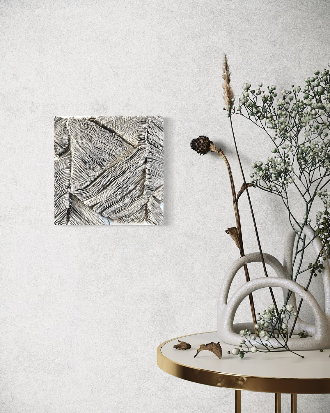 Witte tafel met een vaas met gedroogde bloemen en takken, een witte muur met een kunstwerk van textuur, en een gedroogde bloem op tafel.