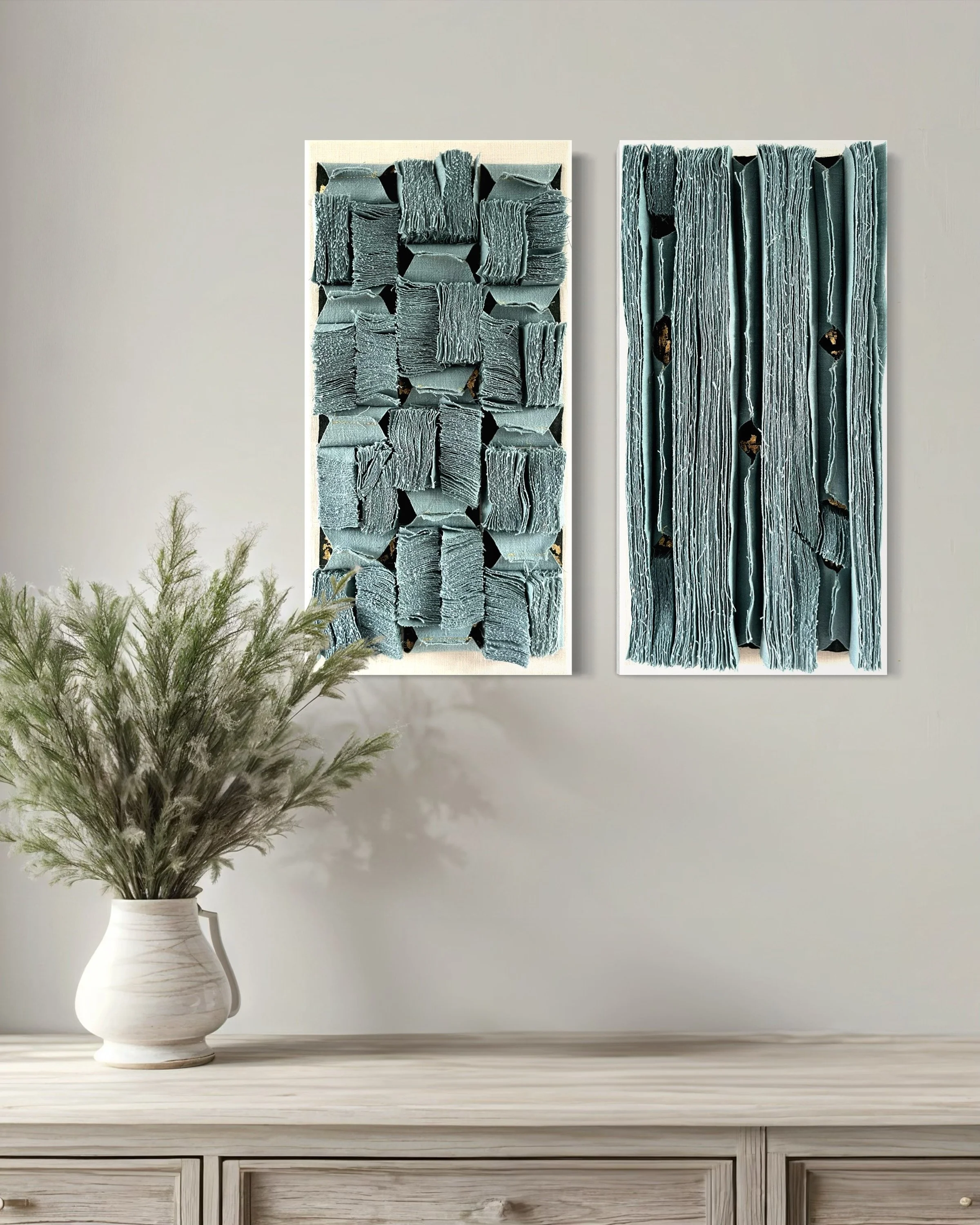 Twee moderne kunstwerken met driedimensionale blauwe textuurelementen hangen aan een lichte muur, met een witte vaas met groene planten op een houtkleurige tafel eronder.