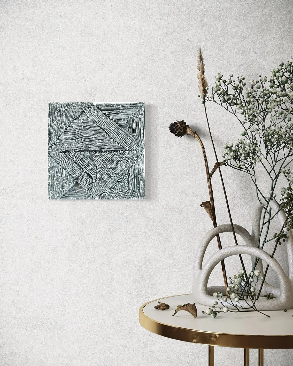 Witte vaas met takken met kleine witte bloemen en enkele gedroogde bladeren, naast een ronde tafel met een gouden rand en een abstract wit beeld op de muur.