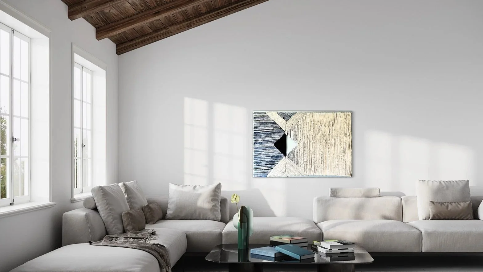 Een lichte woonkamer met een witte bank, een vaas met een blad en boeken op een salontafel, twee grote ramen en een abstract kunstwerk aan de muur, houten plafond.