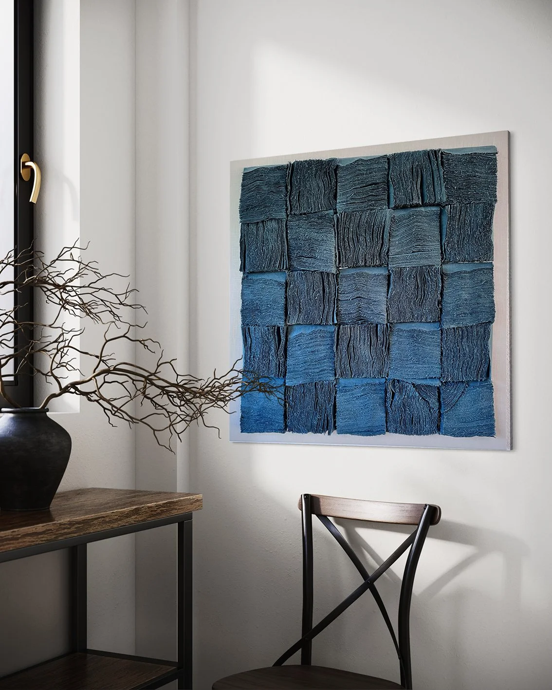 Wanddecoratie bestaande uit 25 geneste stukken in blauw, hangend op een witte muur in een interieur met een houten tafel met een zwarte vaas en een tak en een zwart metalen stoel.