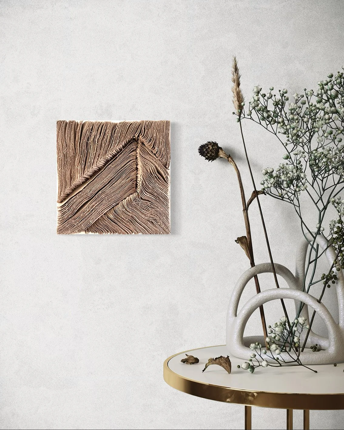 Een witte muur met een abstract kunstwerk en een vaas met gedroogde bloemen en bladeren op een ronde tafel met een goudkleurige rand.