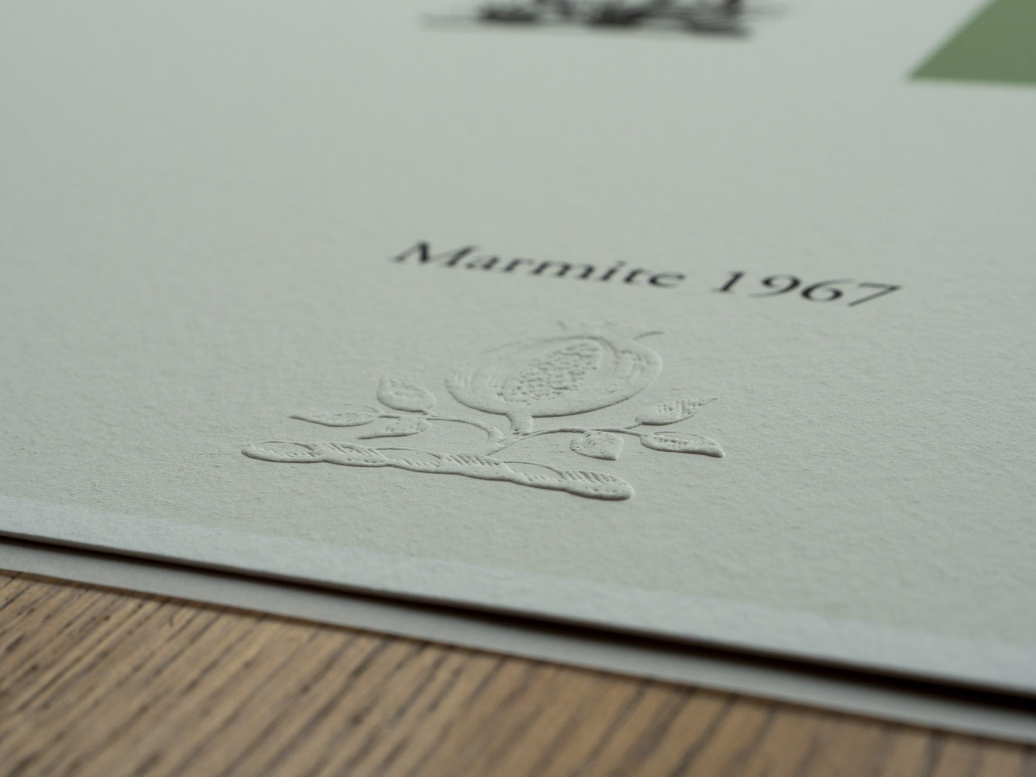 Close-up of embossed text on white paper that reads 'Maritime 1967' with a subtle embossed design of a boat and decorative elements beneath the text. The paper is placed on a wooden surface.
