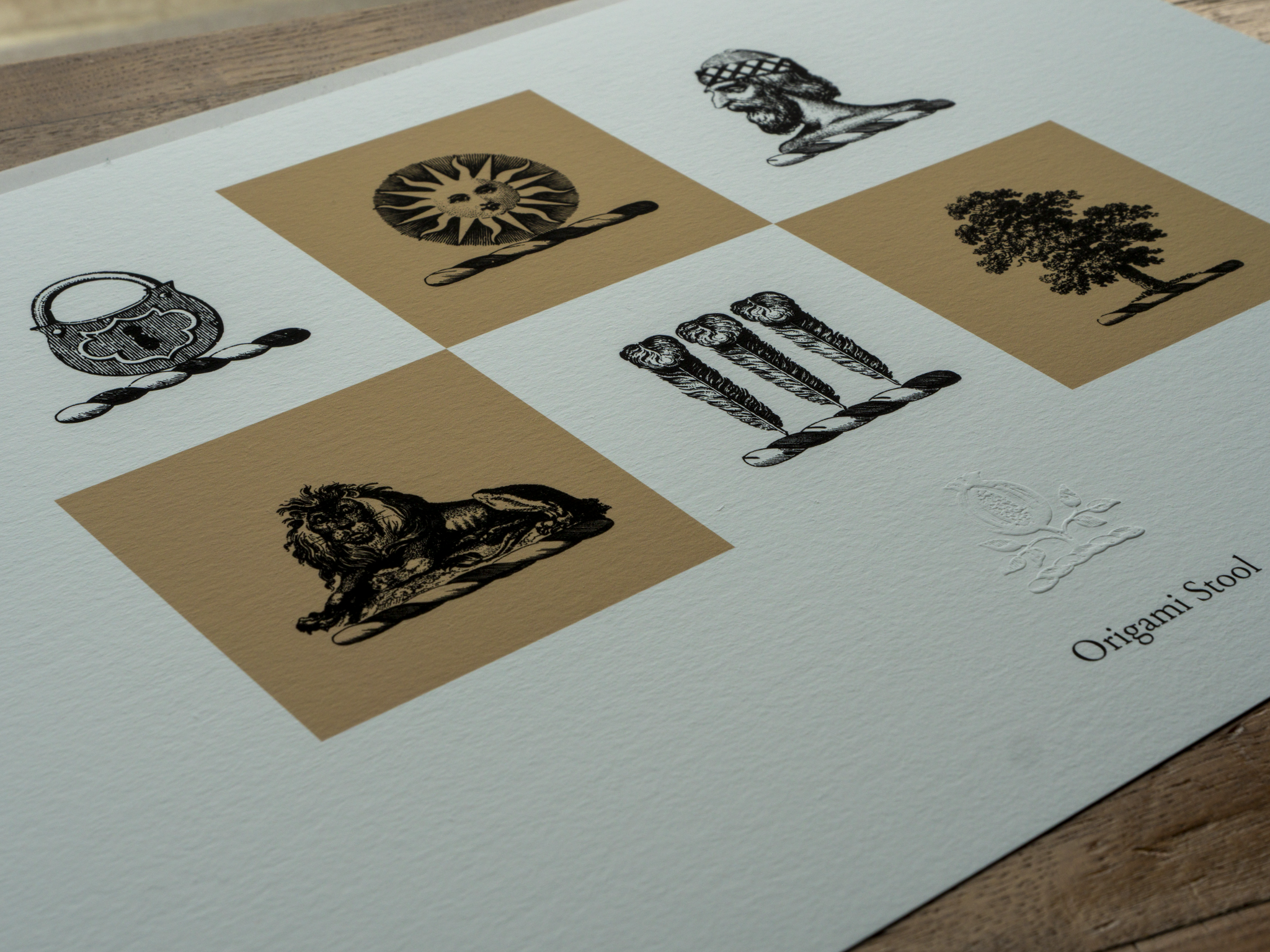 A printed sheet with six black-and-white illustrations of various symbols and objects, each placed on an ochre-coloured square background, arranged on a white sheet of paper on a wooden surface.