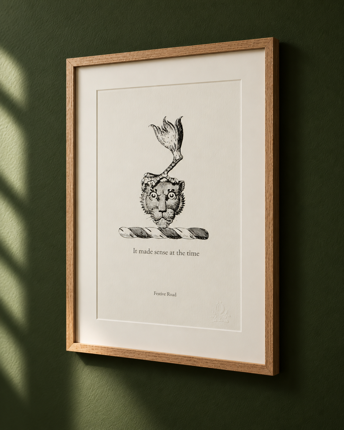 A framed illustration of a lion's head with a fish tail instead of a body, hanging on a green wall. The drawing is accompanied by the text, 'It made sense at the time, Festive Road.'