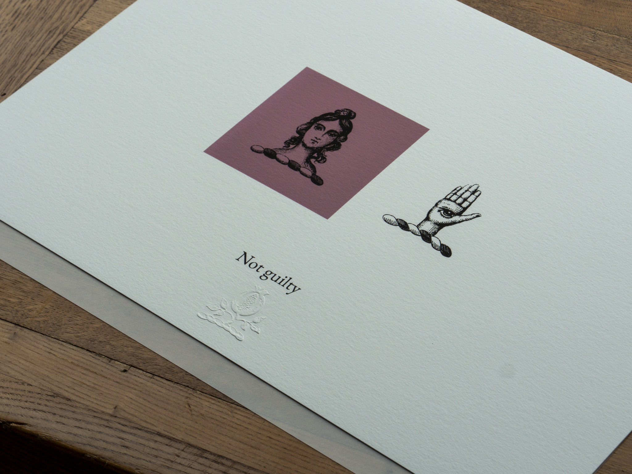 A printed document with a black ink illustration of a woman's bust, positioned within a Rose madder square background, and a smaller illustration of a hand ron textured white paper on a wooden surface.