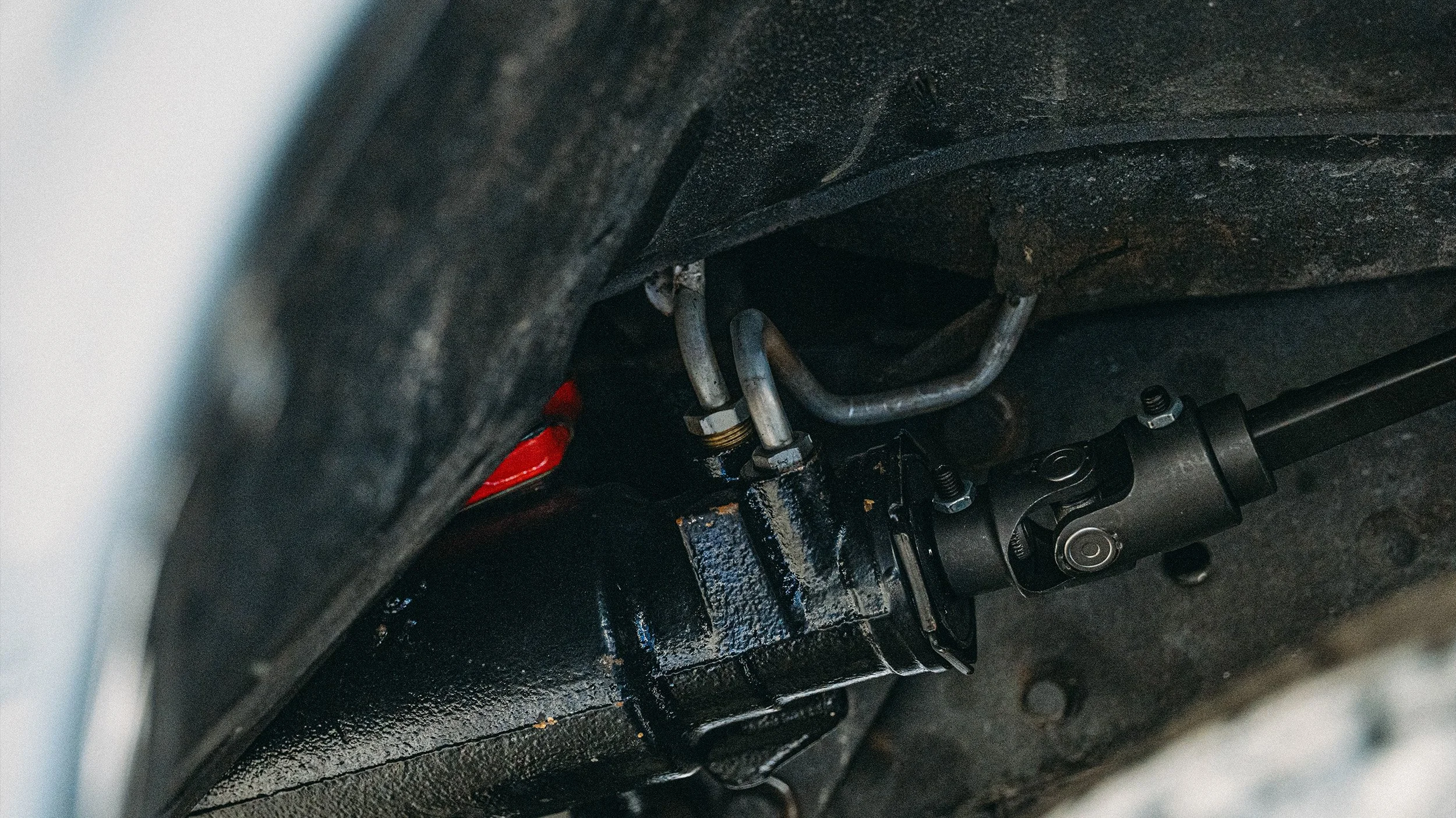 Underneath a vehicle showing a steering component and metal tubes, with black and metallic parts and mounting hardware.