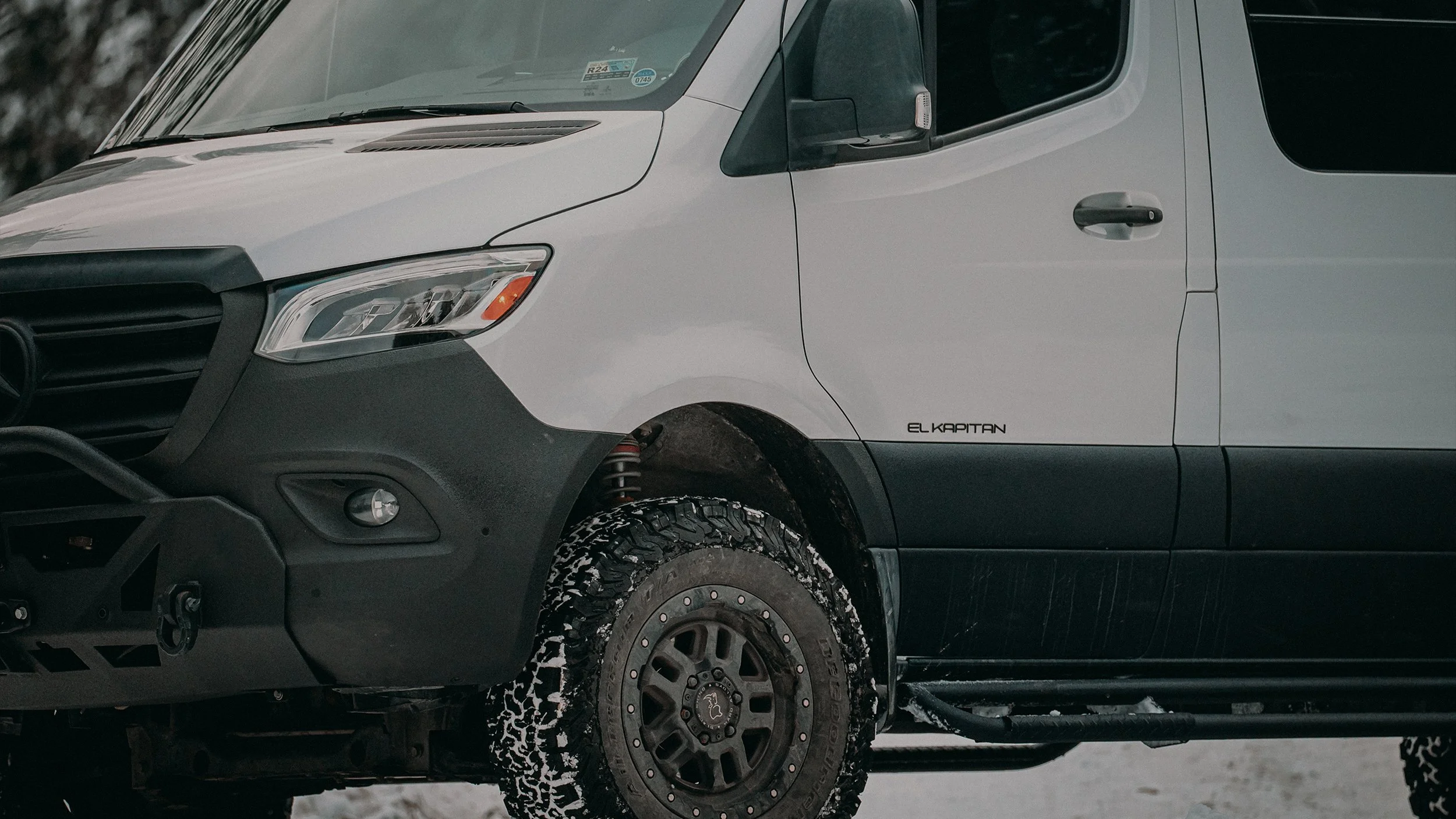 Front right side of a white Mercedes-Benz van with black bumper and tire, parked in snowy environment, with visible suspension and wheel details.