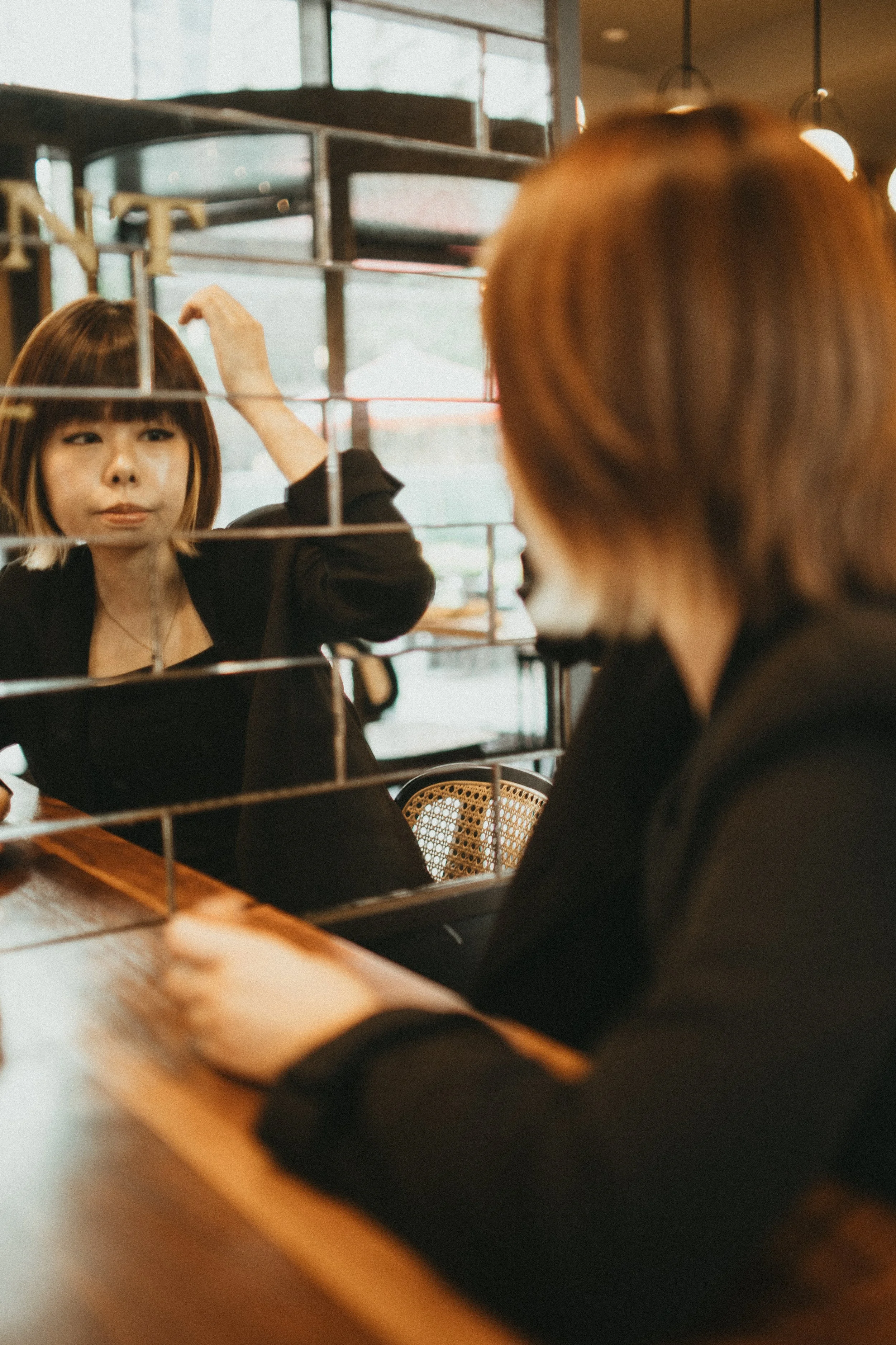 A woman is looking at herself in a mirror, adjusting her hair in a café or restaurant setting.