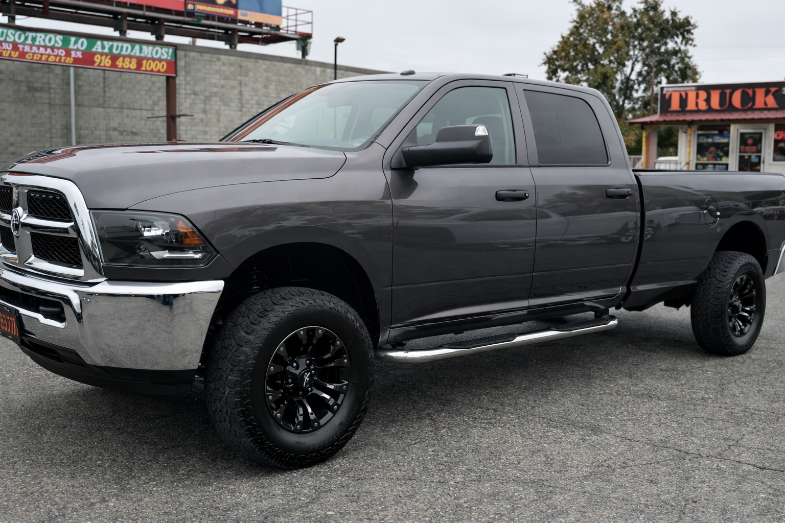 A black pickup truck parked on a street with a truck dealership and a restaurant in the background.