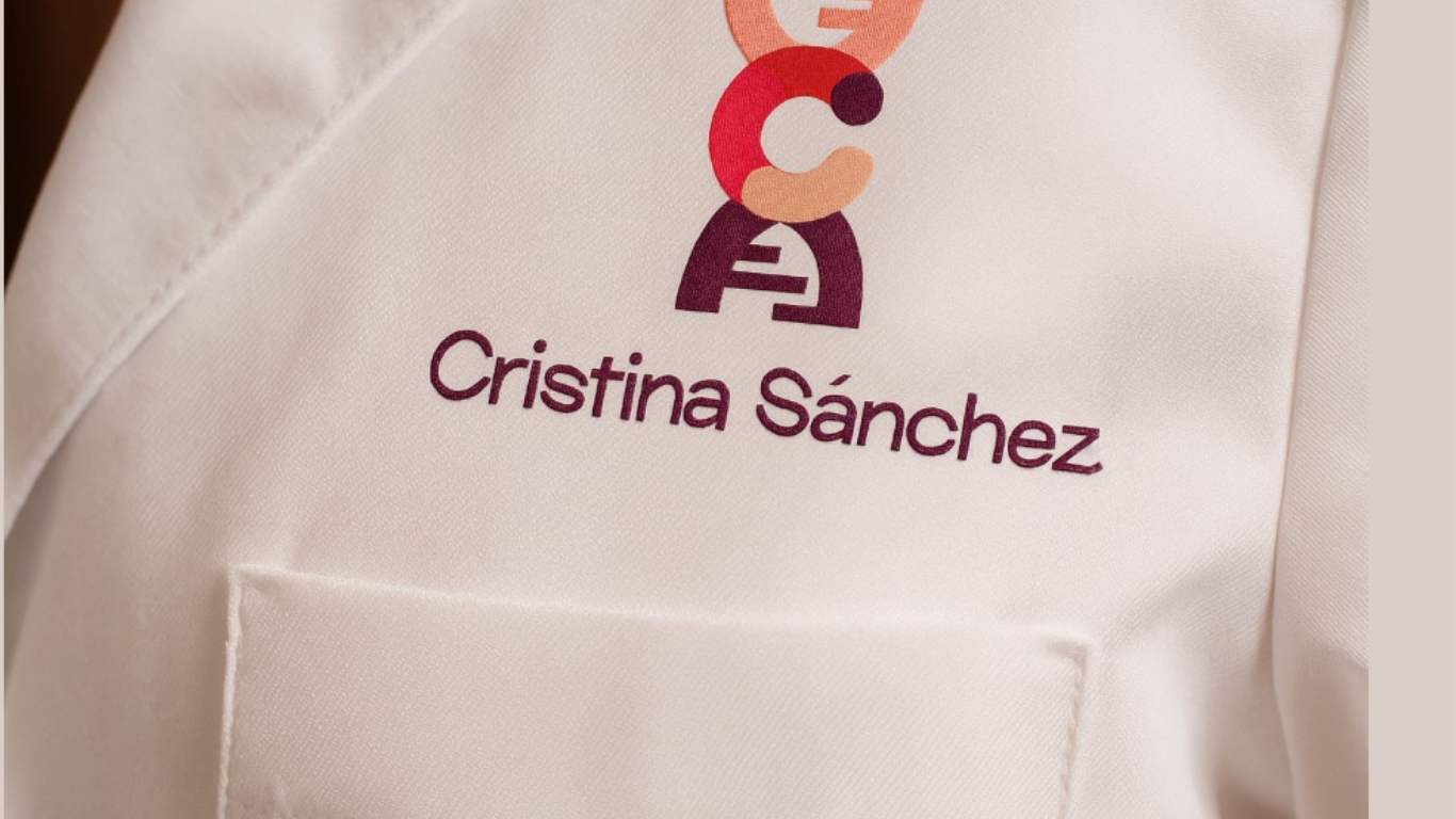 Bata blanca con logotipo colorido y el nombre 'Cristina Sánchez' impreso en morado.