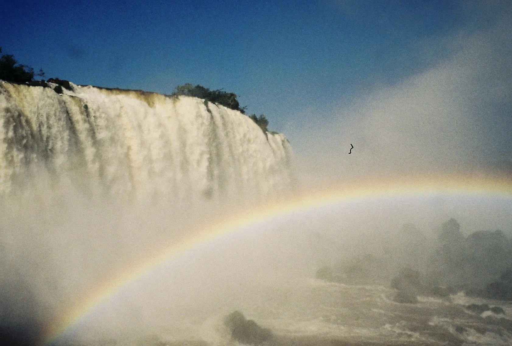 Wasserfall mit Regenbogen im Vordergrund und Himmel im Hintergrund.