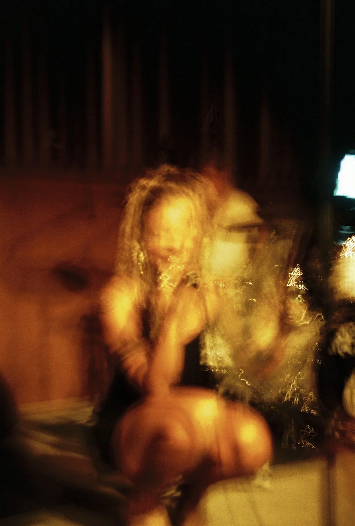 Eine Frau mit langen, lockigen Haaren sitzt im Dunkeln, während sie auf ein Smartphone schaut. Die Bildqualität ist unscharf und zeigt Bewegung.