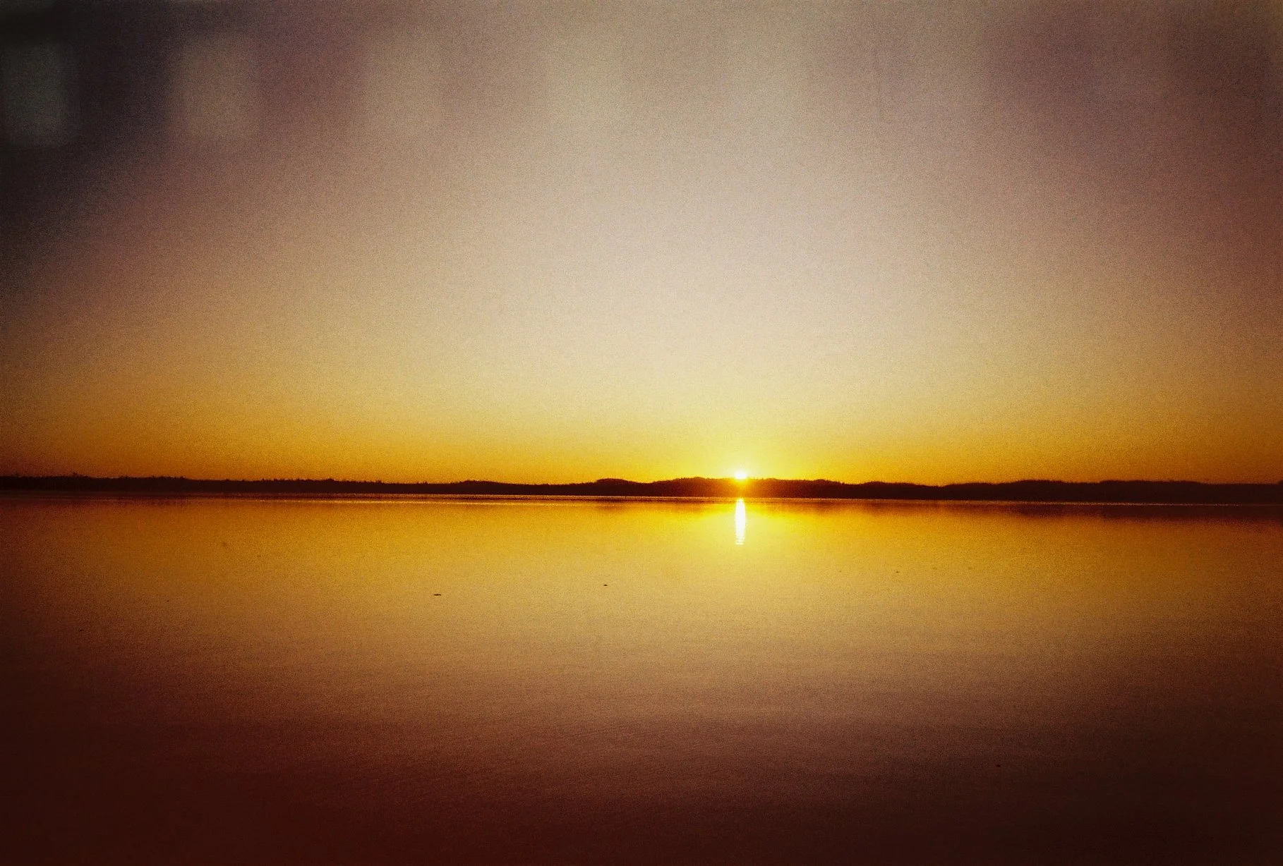 Sonnenuntergang über einem ruhigen See mit spiegelndem Wasser.