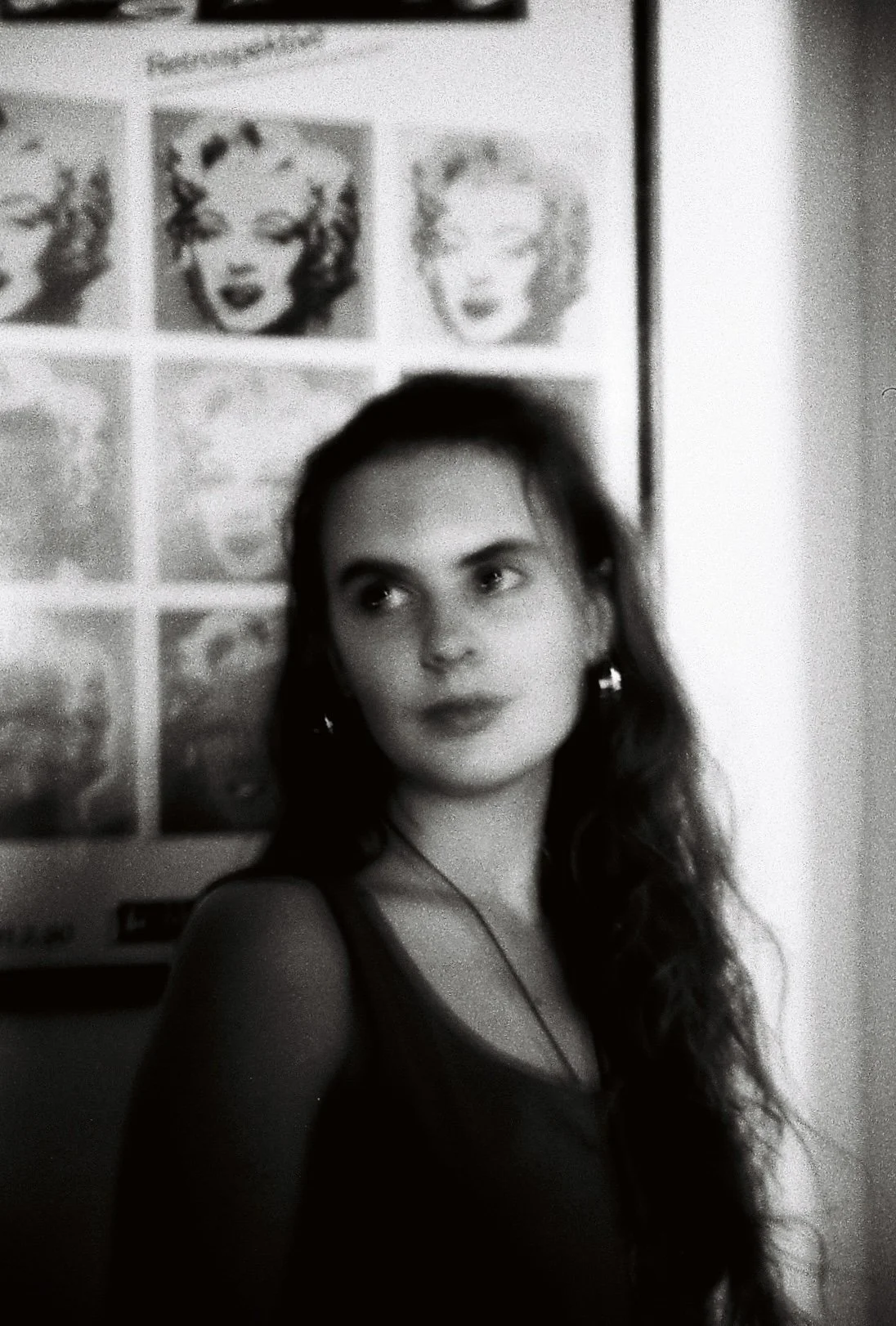 Schwarz-weiß-Foto eines jungen Mädchens mit langen, gewellten Haaren, das vor einem Poster mit Bildern des berühmten Marilyn Monroe steht.