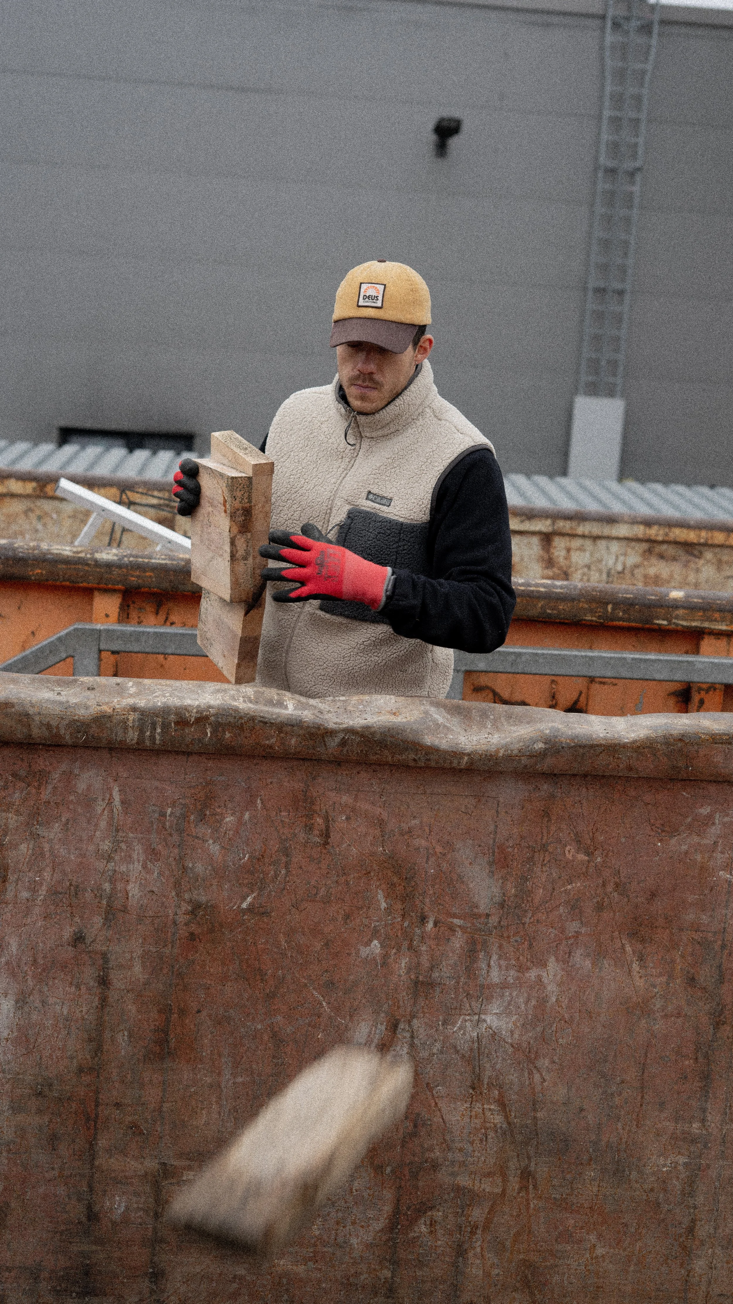 Ein Mann arbeitet auf einer Baustelle und hält einen Ziegelstein in der Hand, während er Schutt einen Container wirft.