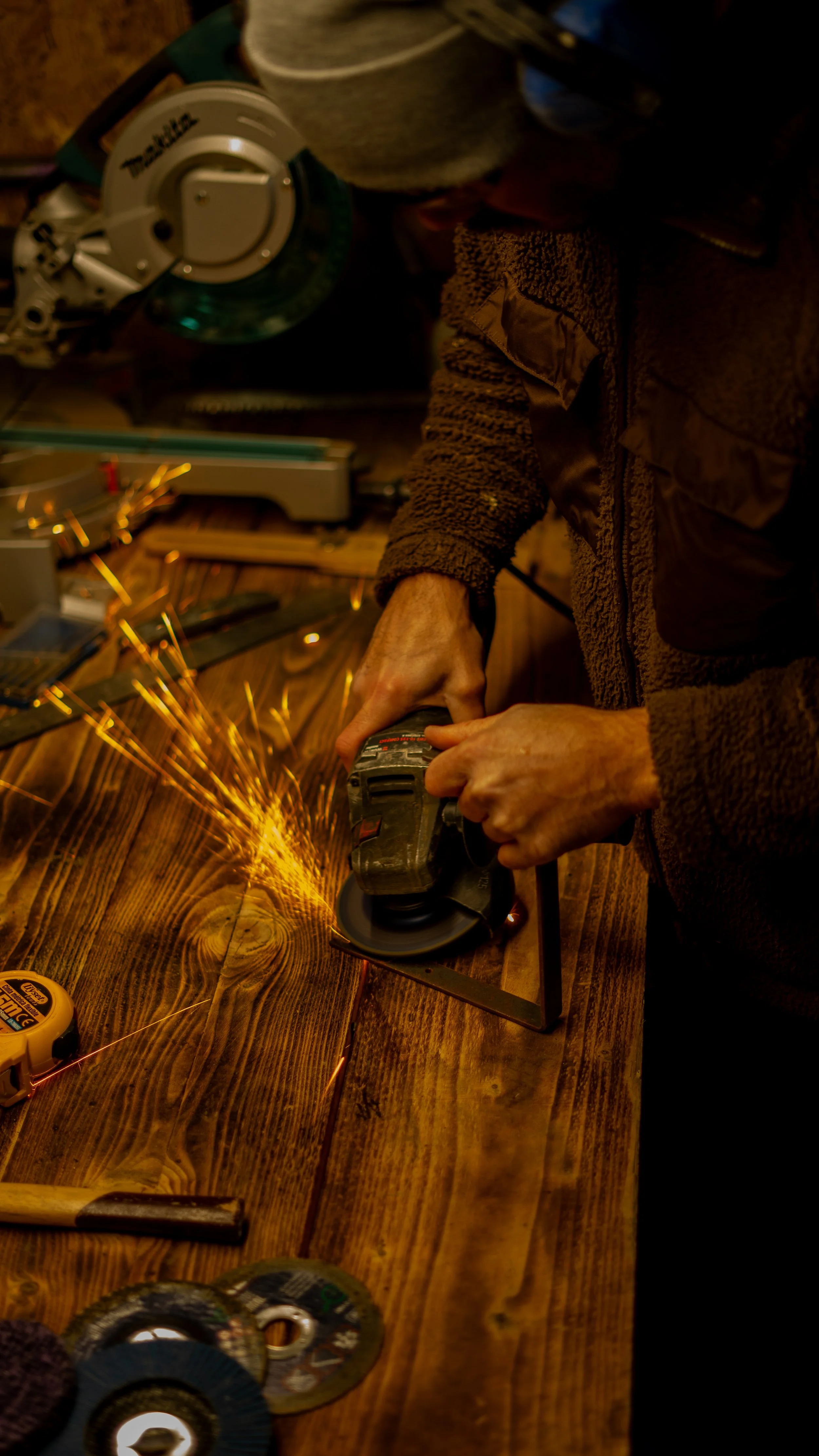 Person benutzt eine Flex, um ein Stück Metall auf einem Holztisch zu bearbeiten, wobei Funken fliegen.