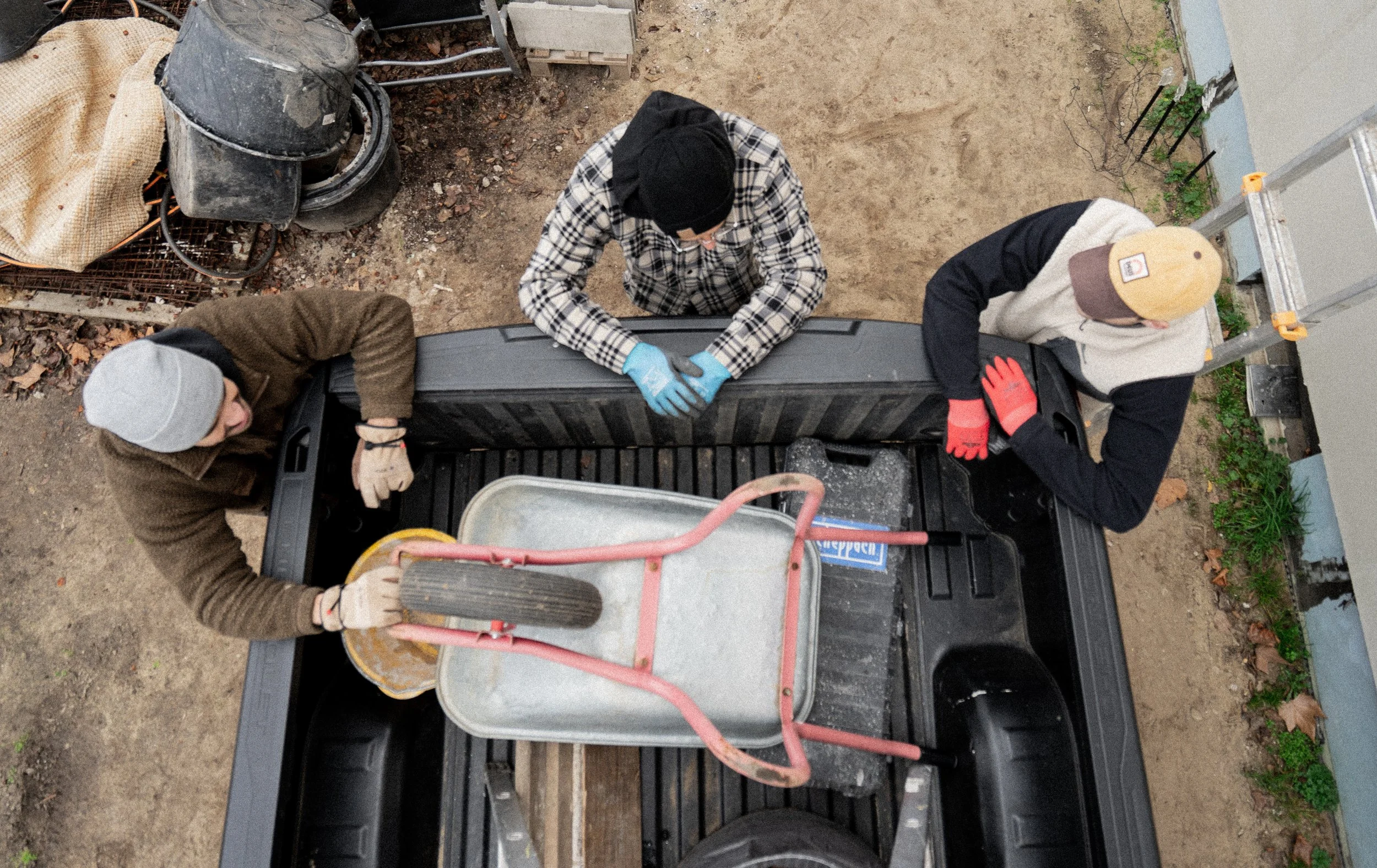 Drei Personen arbeiten auf der Ladefläche eines Lastwagens. Sie tragen Arbeitshandschuhe und benutzen Werkzeuge, um eine Aufgabe zu erledigen.