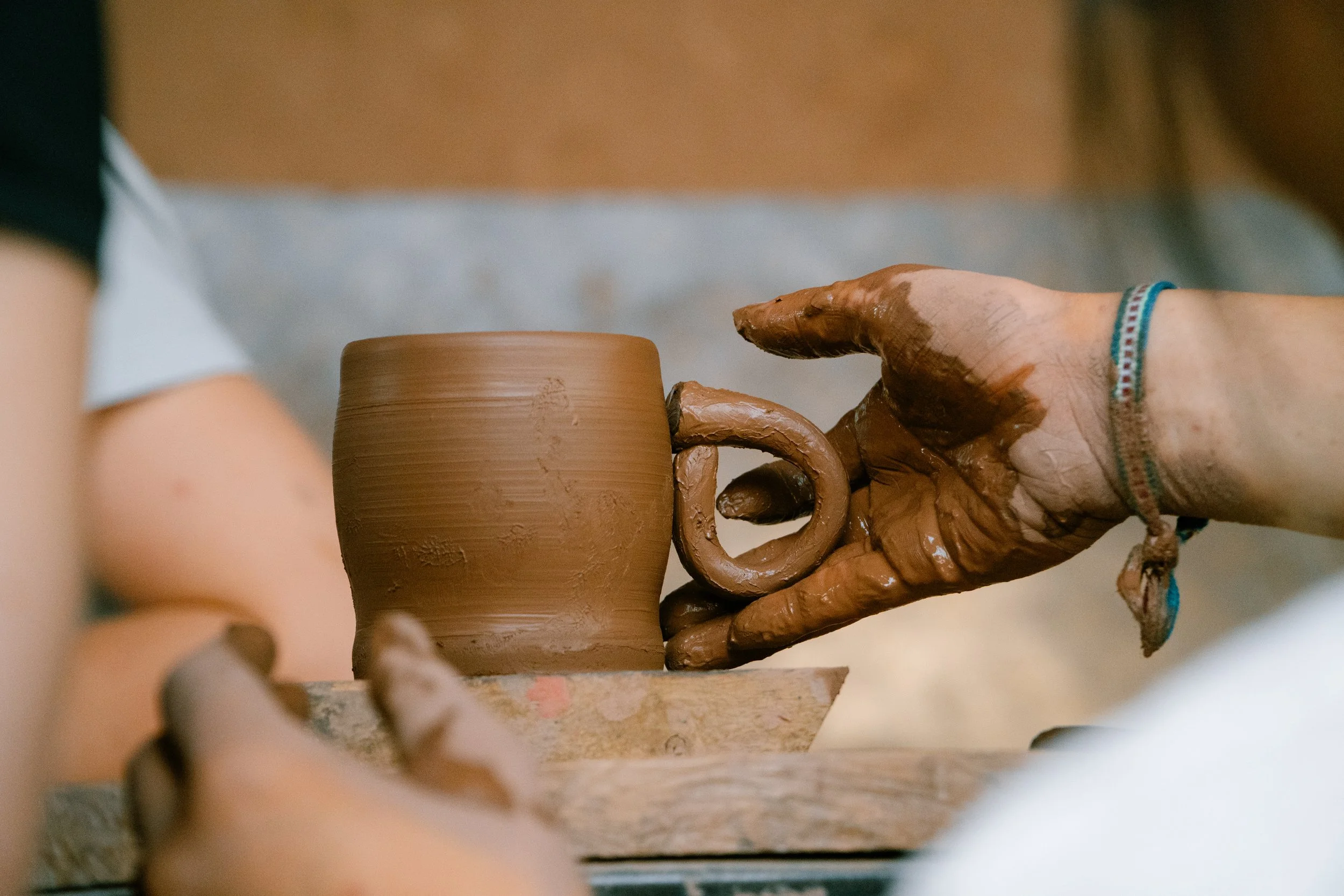 Person shaping a clay mug on a pottery wheel