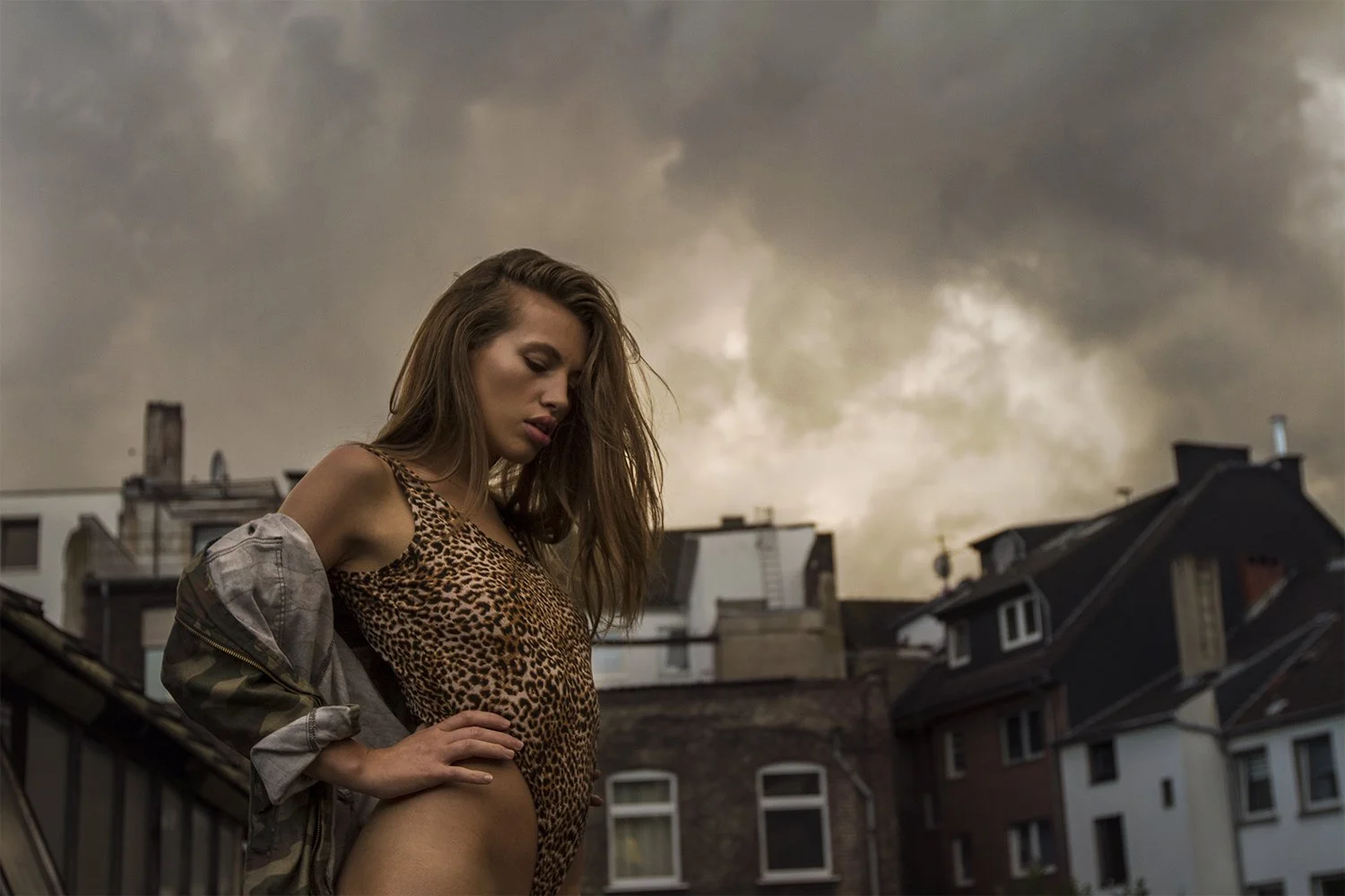 A woman in a leopard print top and camouflage jacket standing on a rooftop with a dark, cloudy sky in the background.