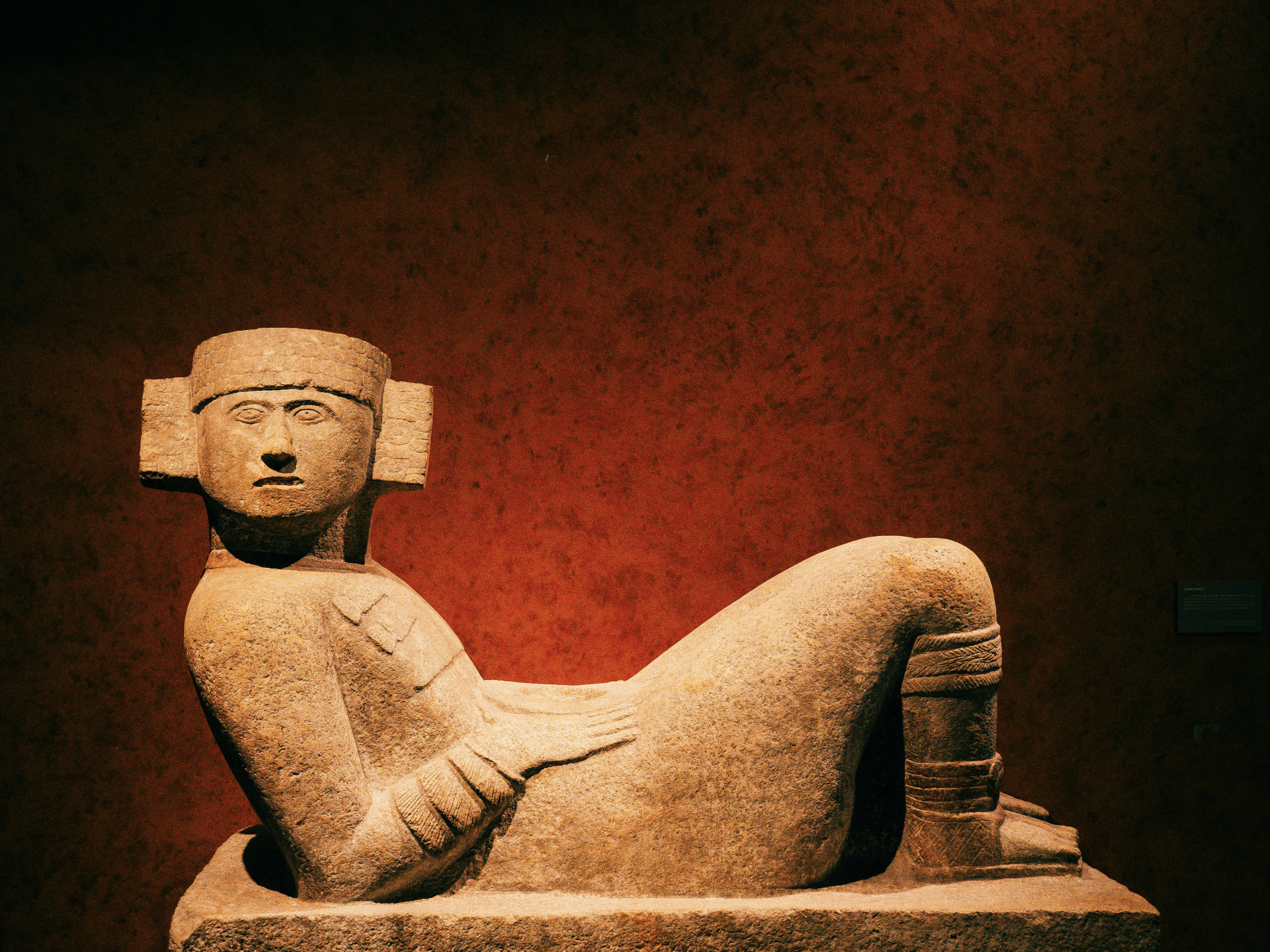 Stone sculpture of a reclining figure with a human face, possibly of ancient origin, displayed in a museum setting.
