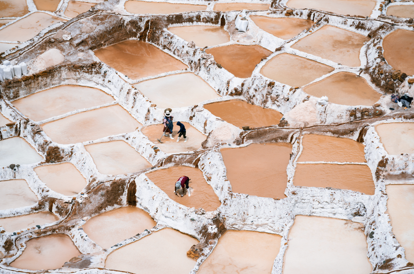 Workers harvesting salt in salt evaporation ponds with pink and white coloration.