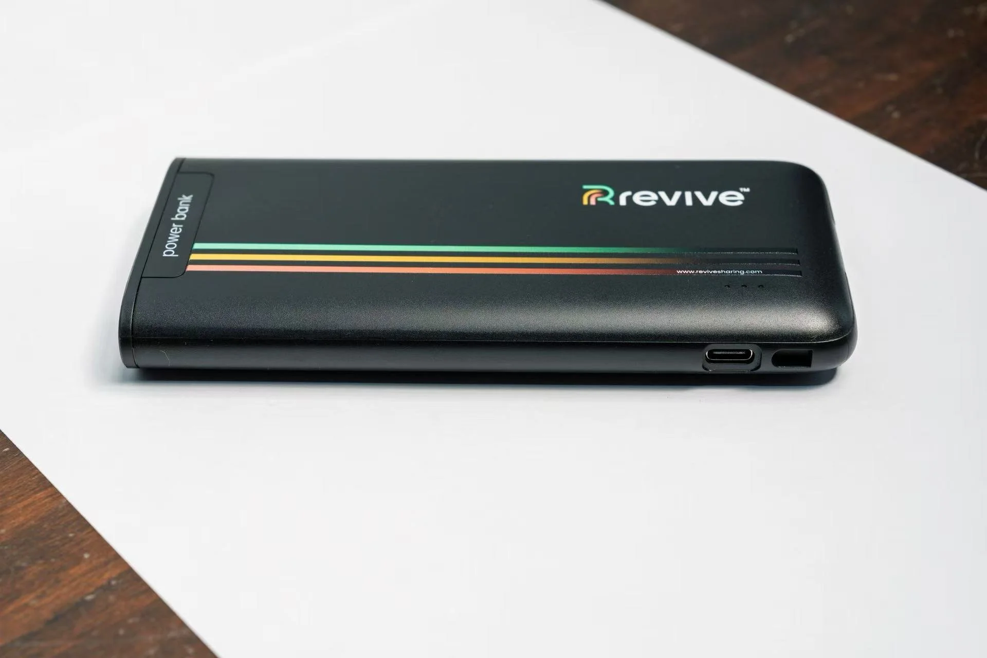 Black portable power bank with the Revive logo, Bluetooth label, and colorful stripes, resting on a white surface.