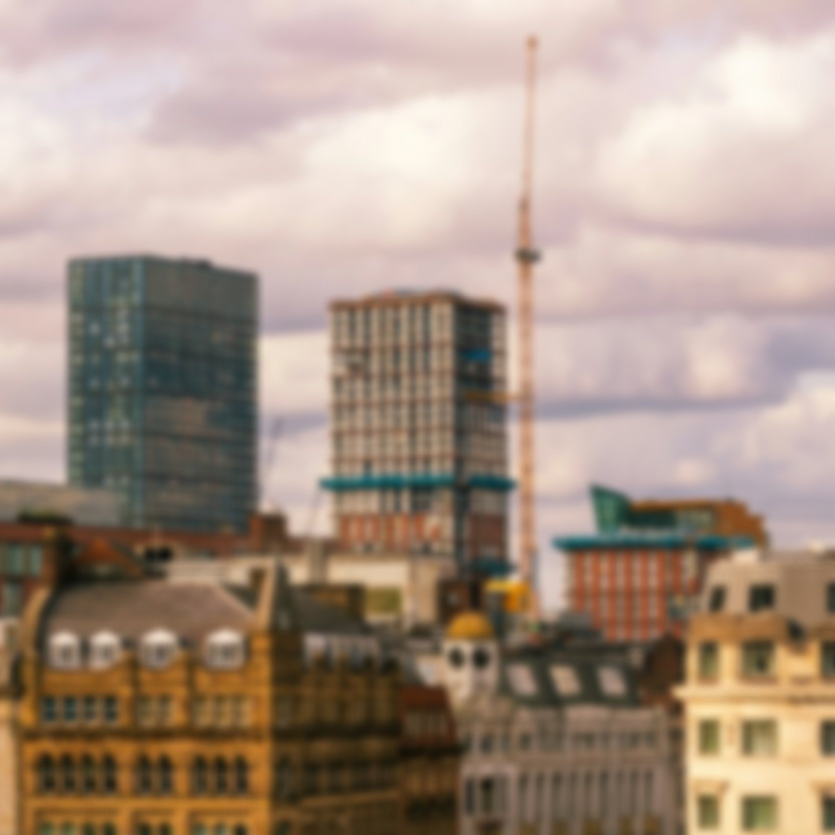 Manchester city skyline with modern high-rise buildings and a construction crane.