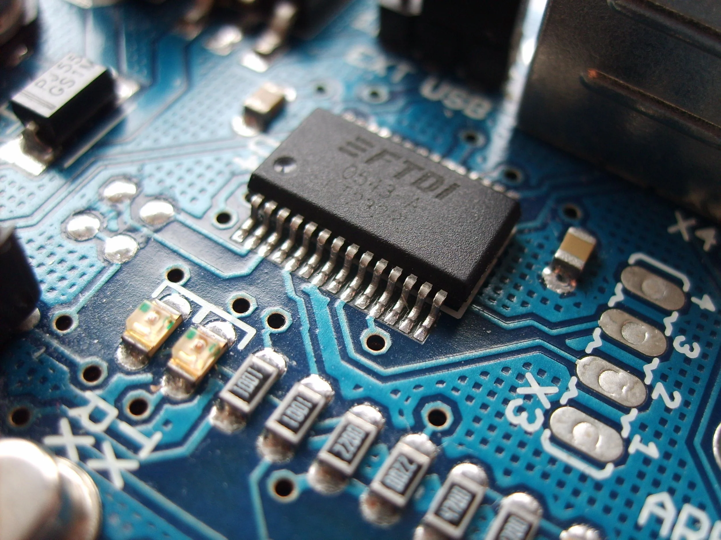 Close-up of a blue printed circuit board with various electronic components including a black integrated circuit chip, small resistors, and capacitors.