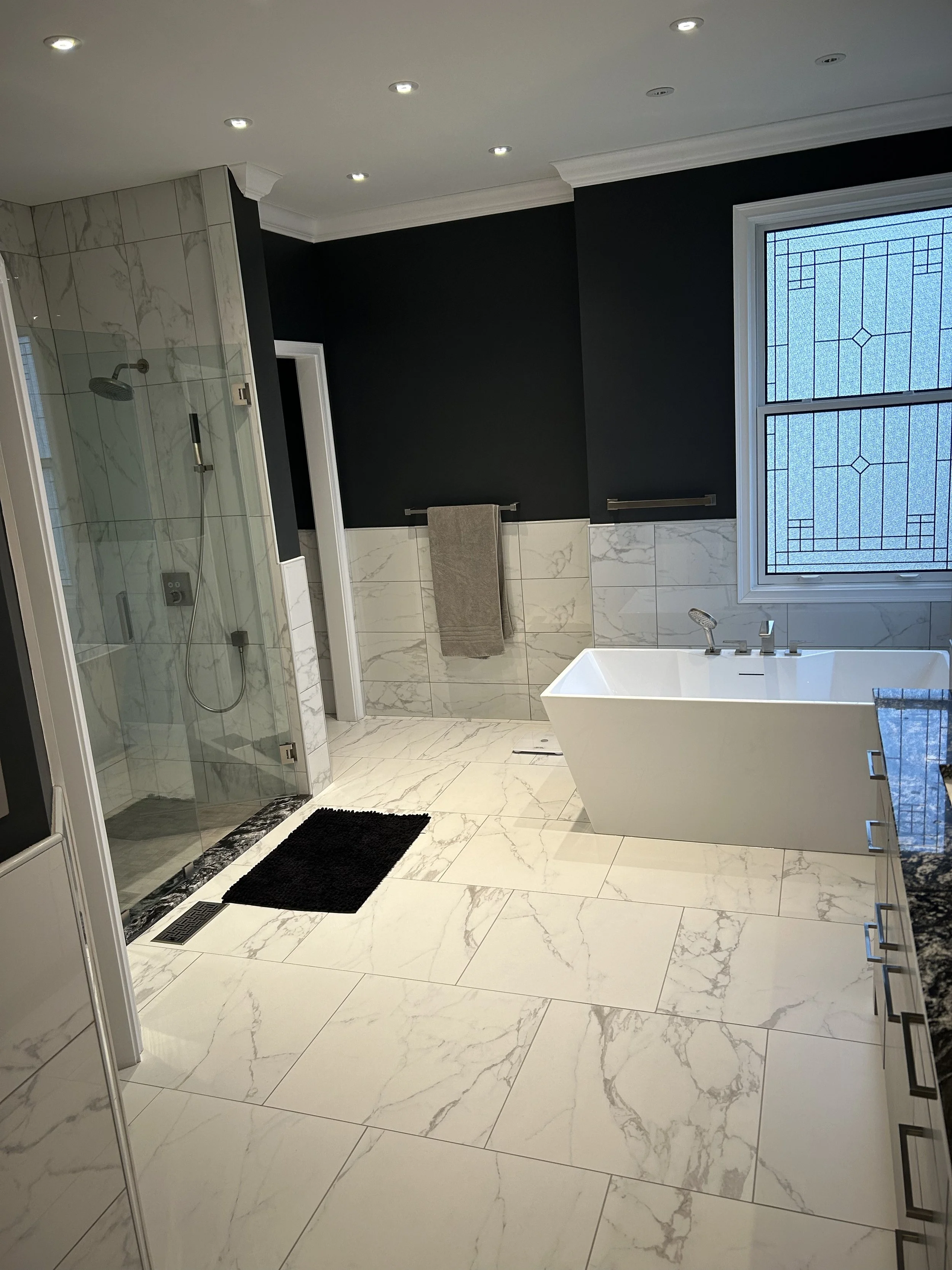 Modern bathroom with a walk-in shower, bathtub, and black walls with marble accents.