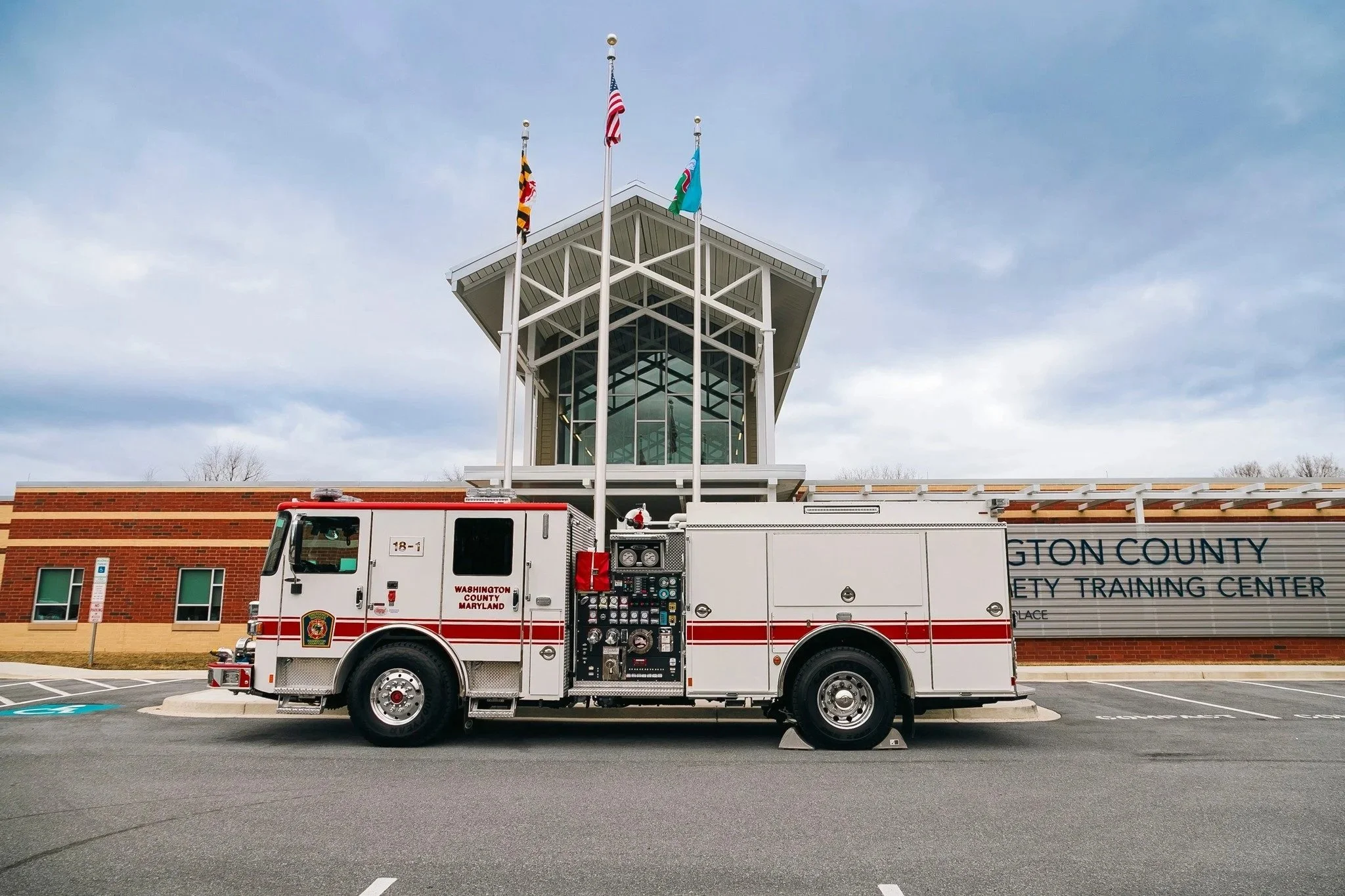 A white firetruck in front of the Washington County Safety Training Center with blue skies and three flags rising up from behind the building. 