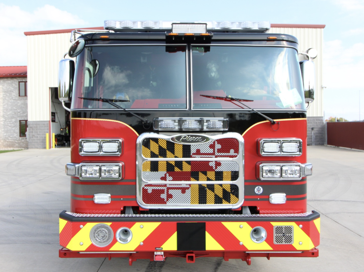 The front of a firetruck with blue skies behind it and a Maryland flag design on the front.