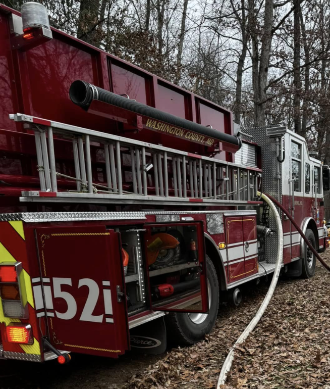 A firetruck in the woods with doors open and a hose extending out from it. 