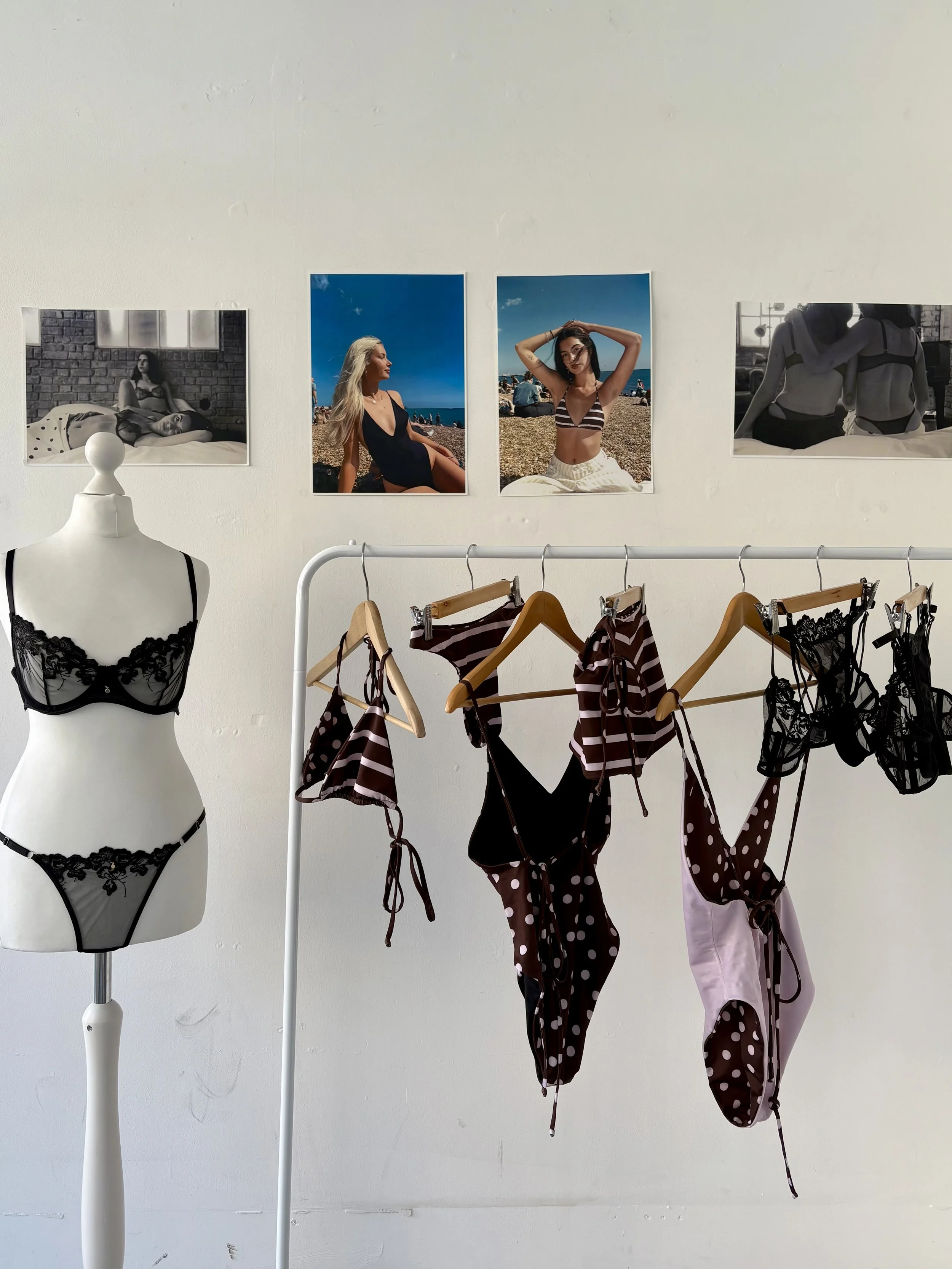 Display of black lace lingerie on a mannequin and a clothing rack with swimwear, with four fashion photos on the wall above.
