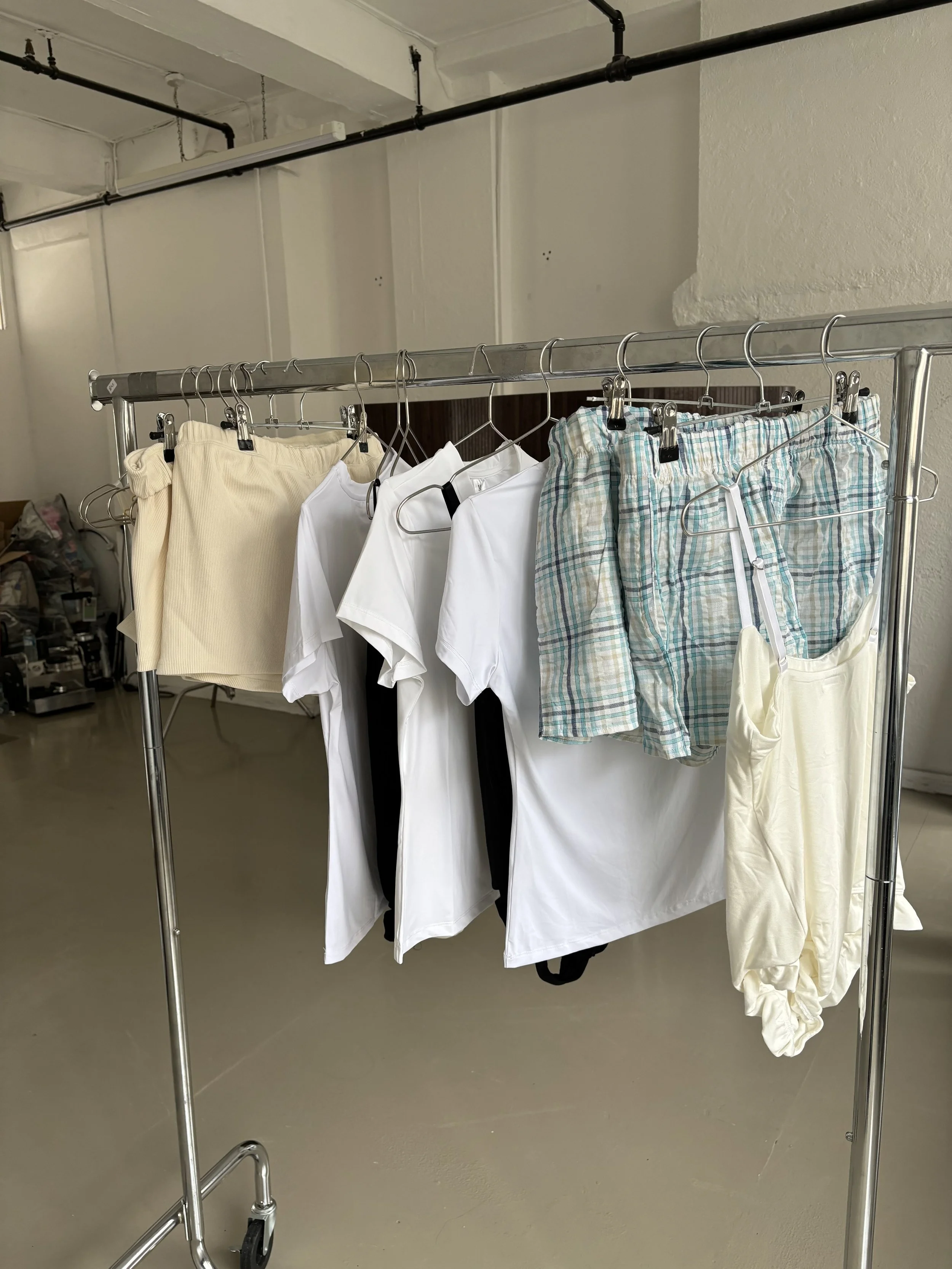 Clothes hanging on a metal rack, including shorts, t-shirts, and a pair of plaid shorts.