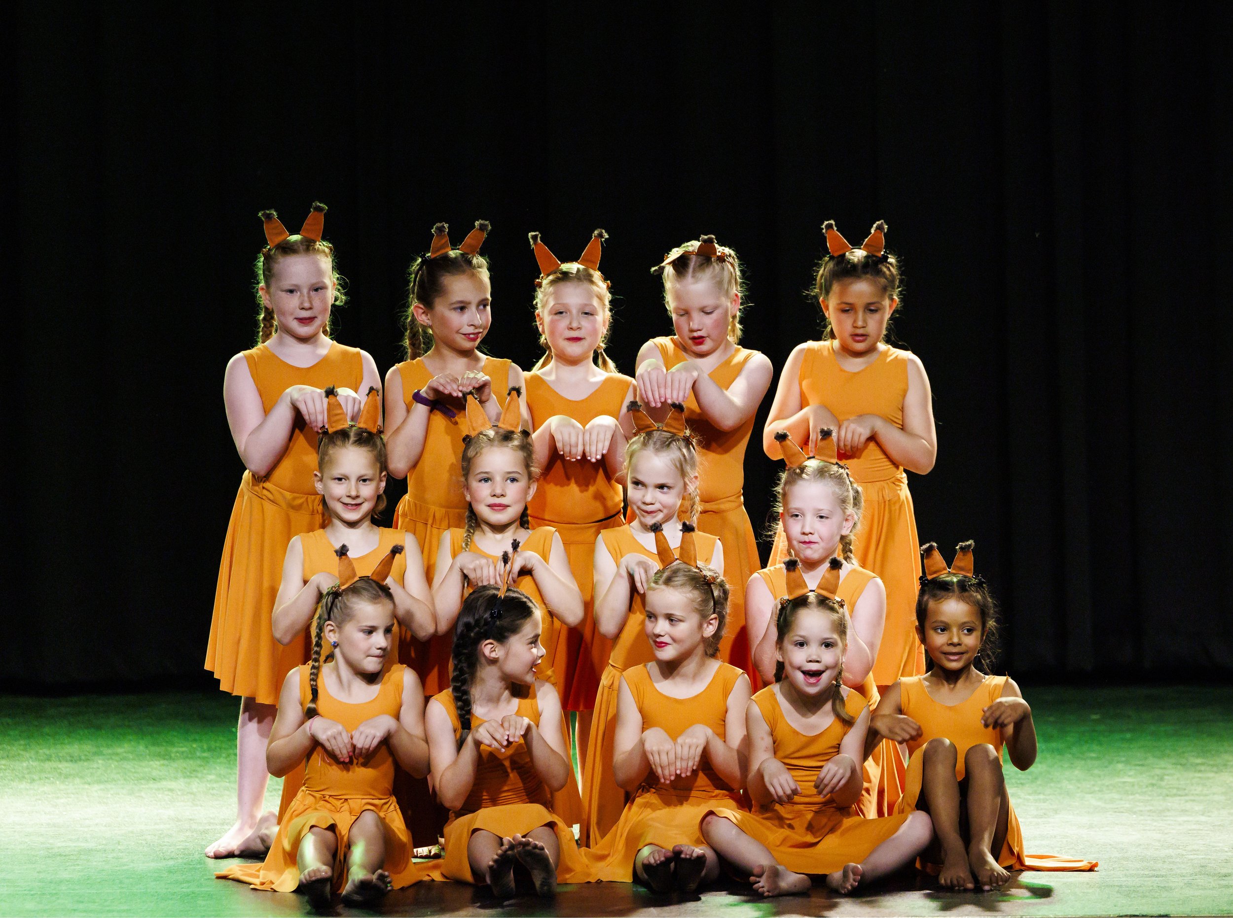 Jonge meisjes in oranje kostuums met konijnenoren maken deel uit van een dansgroep op een podium.