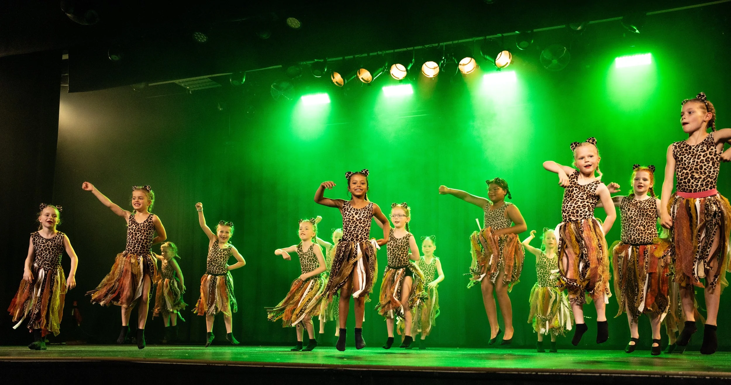 Kinderen voeren een dansoptreden uit op een podium, gekleed in leopard print kostuums.