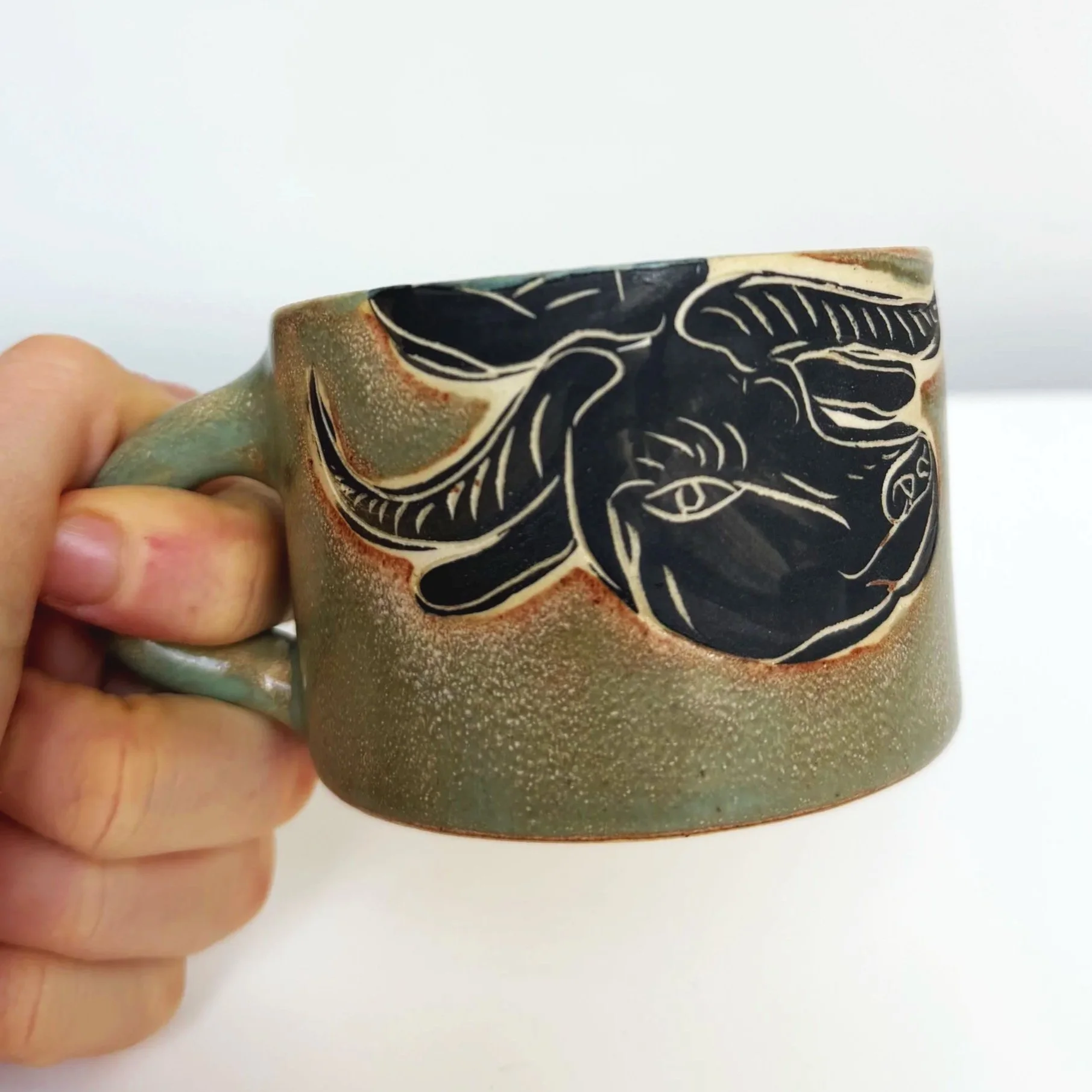 A round ceramic bowl with a glazed interior, with green, brown, and cream colors, held by a hand.