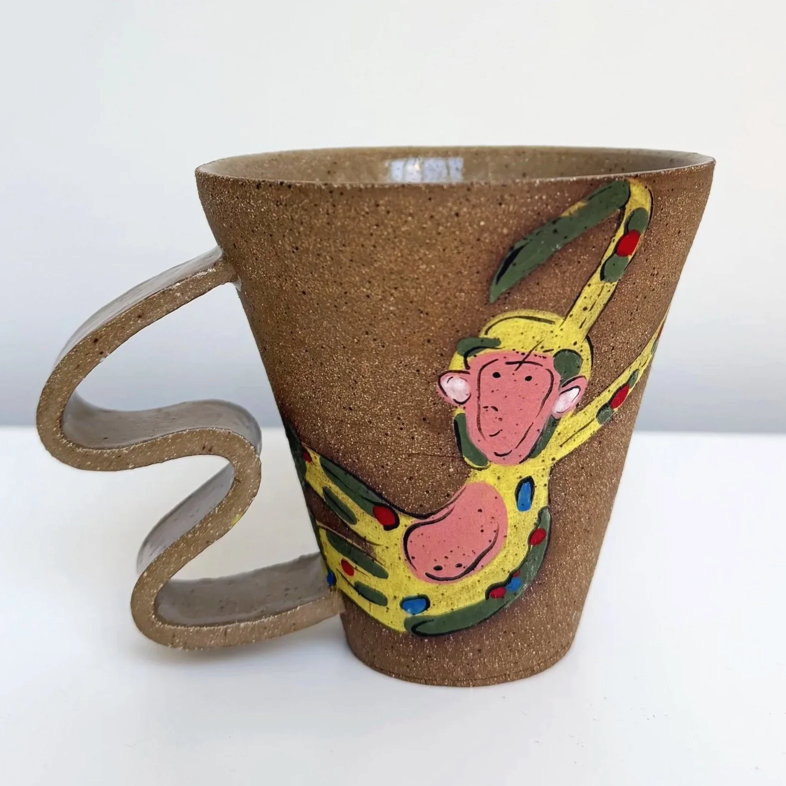 A hand holding a ceramic cup decorated with a painted black and white monkey with a red face.