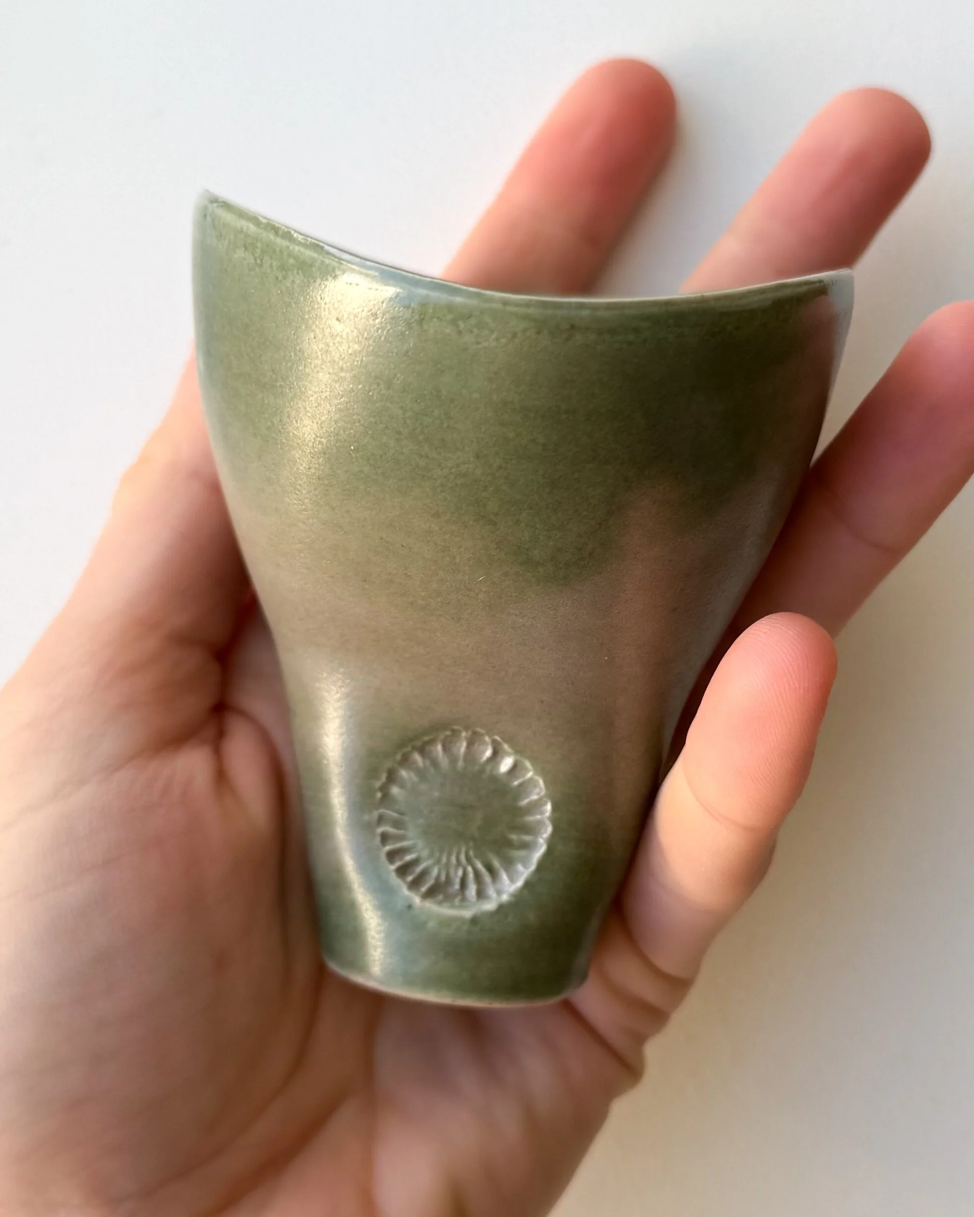 A person's hand holding a green ceramic cup with a decorative pattern near the base.