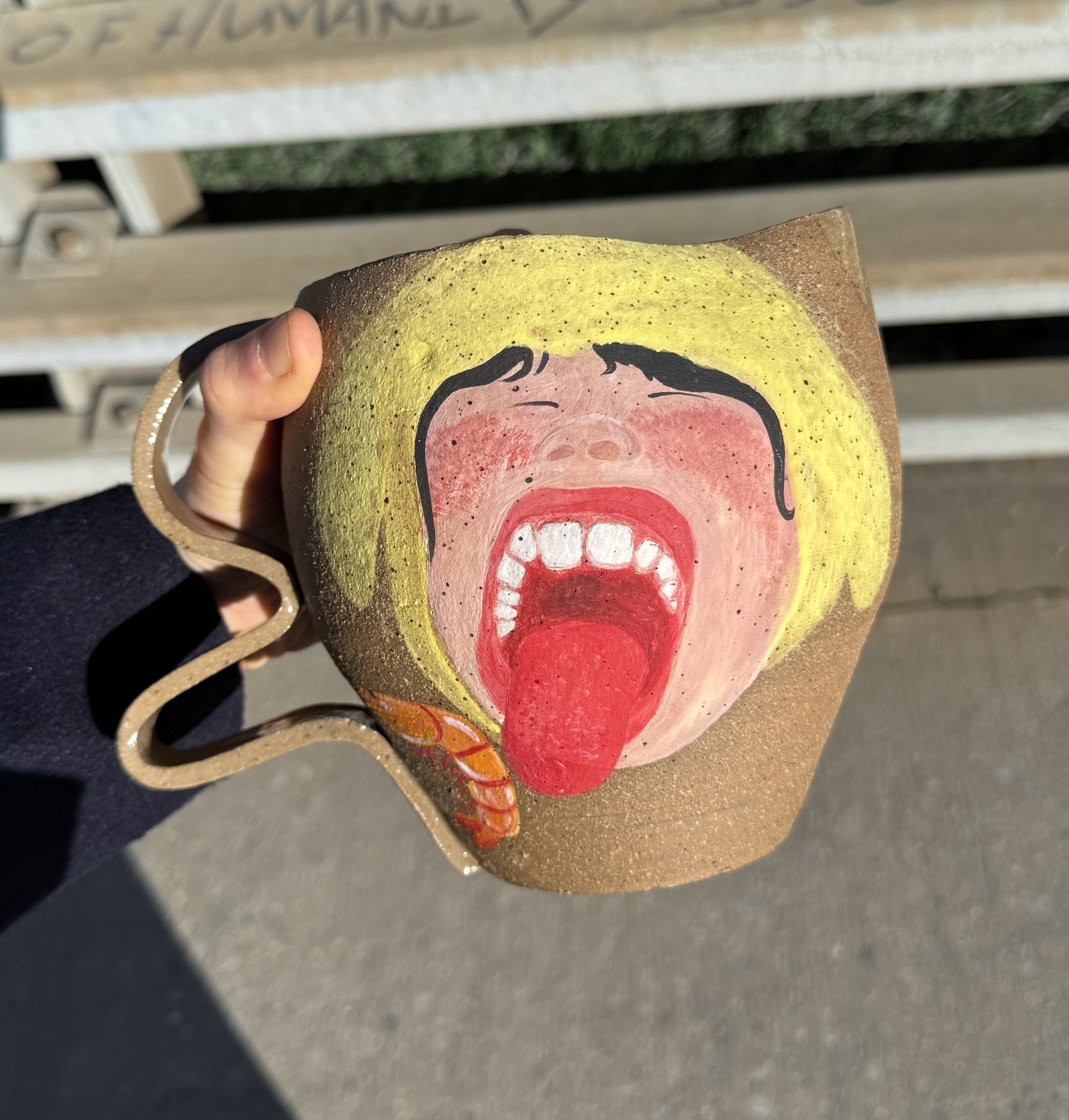 Two ceramic cups with black monkey illustrations and red faces, held in a person's hand against a wooden background.