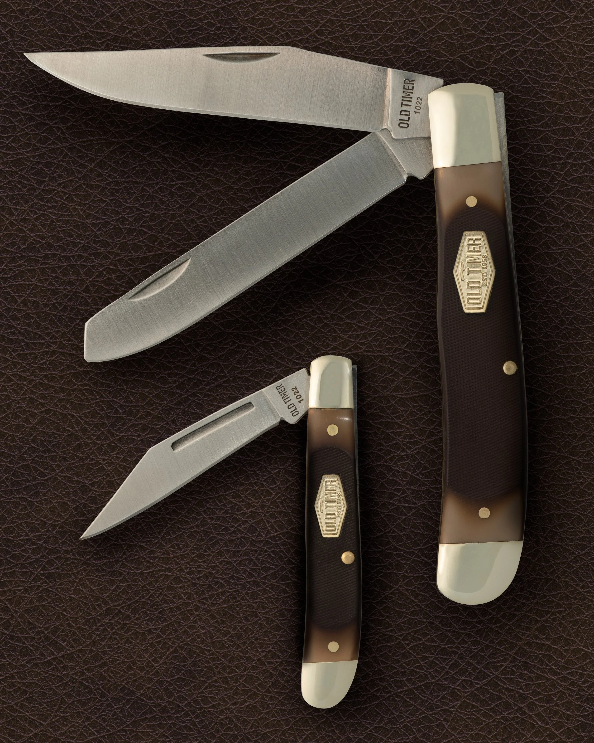 Two pocket knives with black, white, and gray handles, and metal blades resting on a brown textured surface.