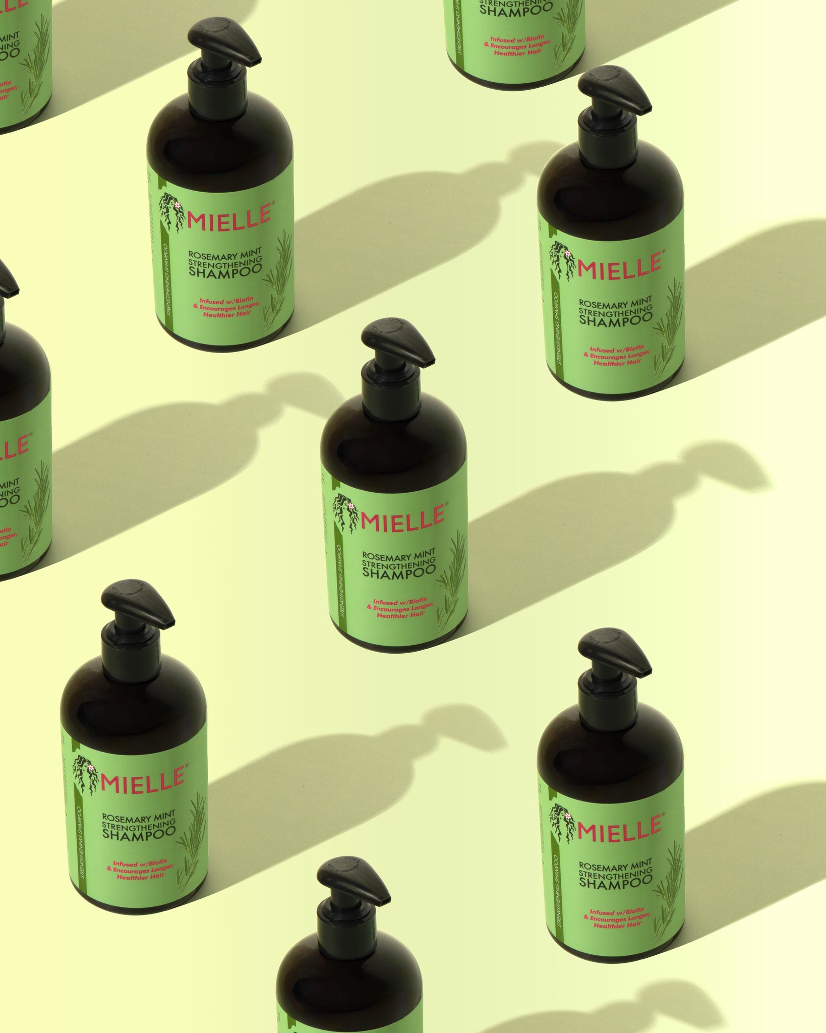 Multiple bottles of Mielle rosemary mint strengthening shampoo arranged on a light yellow surface, with their shadows cast to the side.